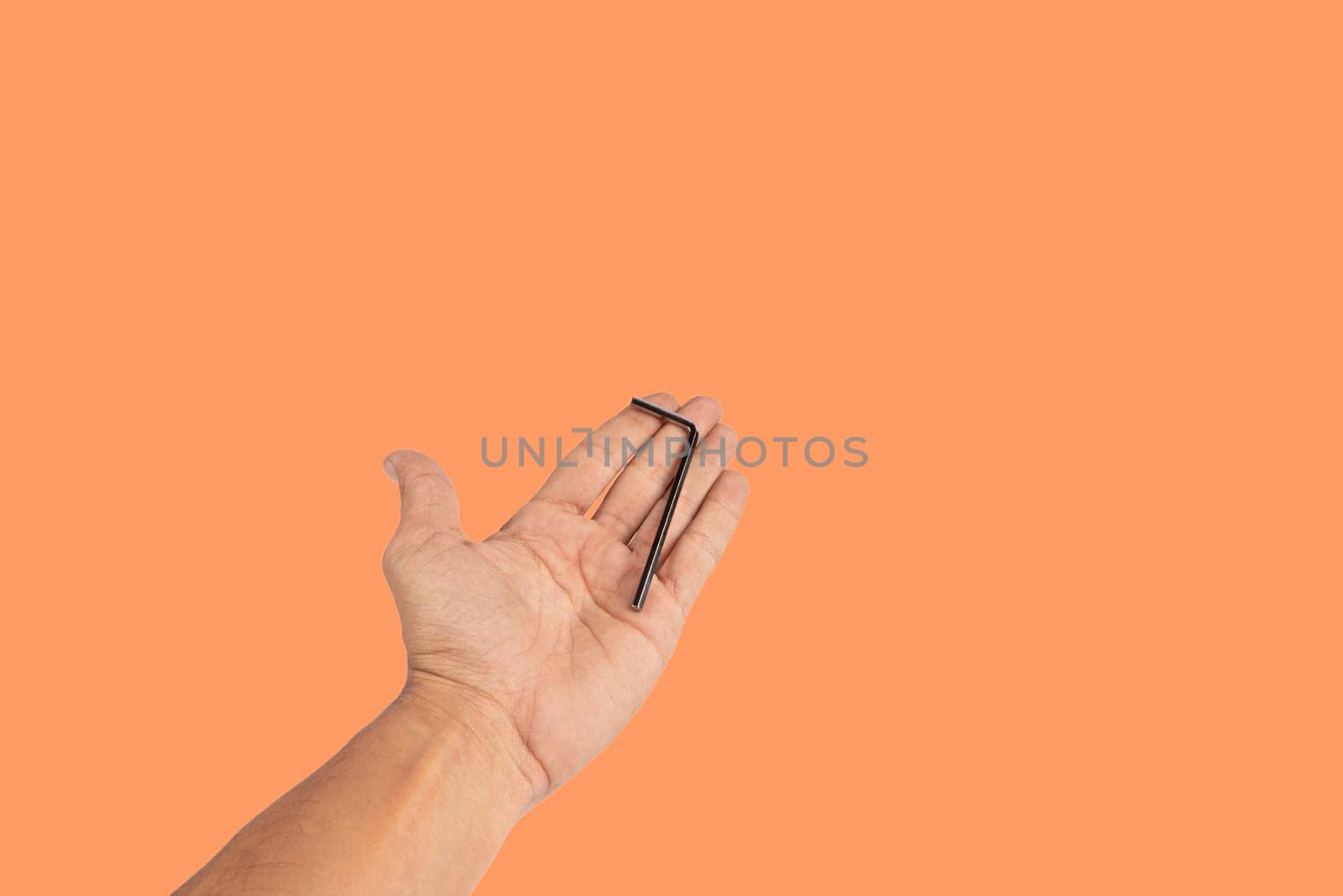 Black male hand holding an allen key isolated on orange background, cutout. High quality photo