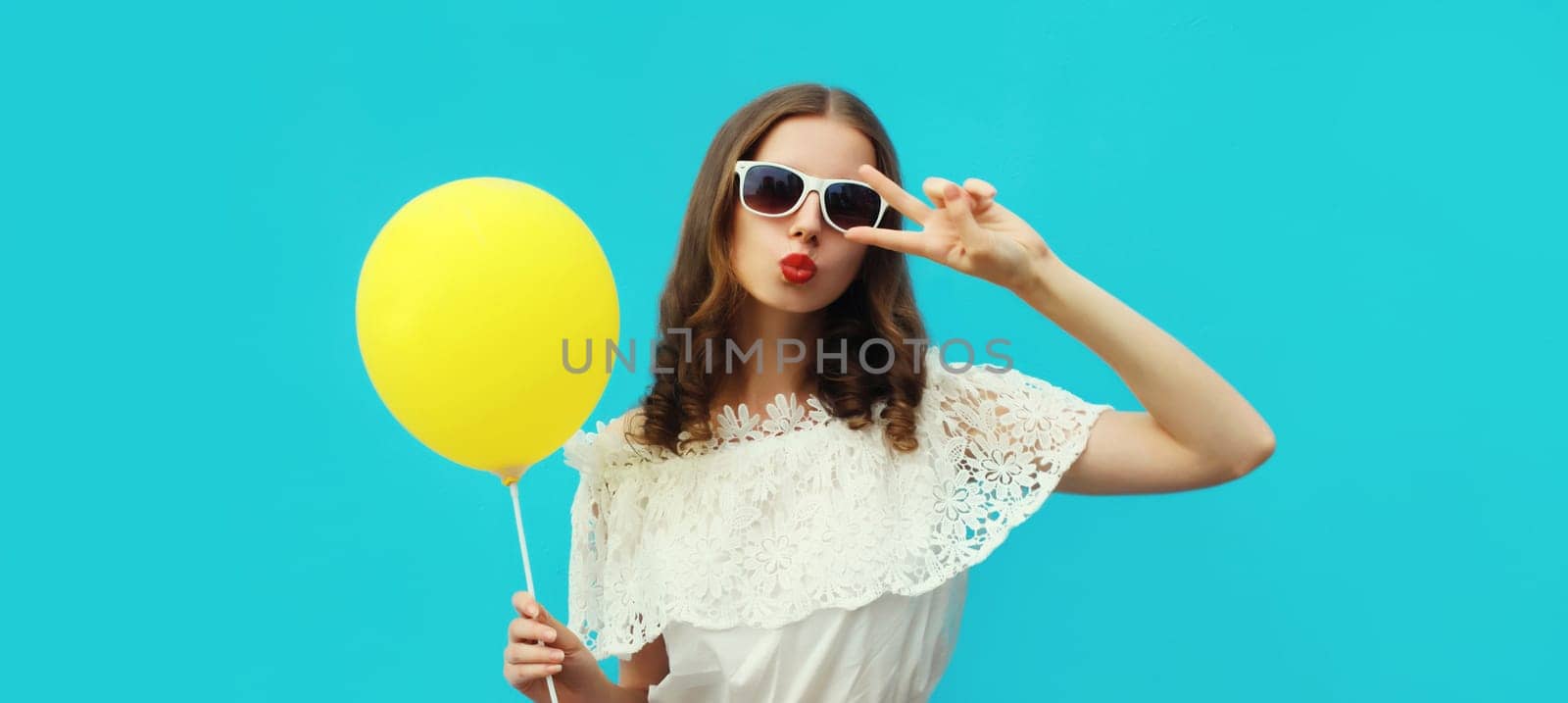 Summer portrait of happy pretty young woman with yellow balloon on blue studio background