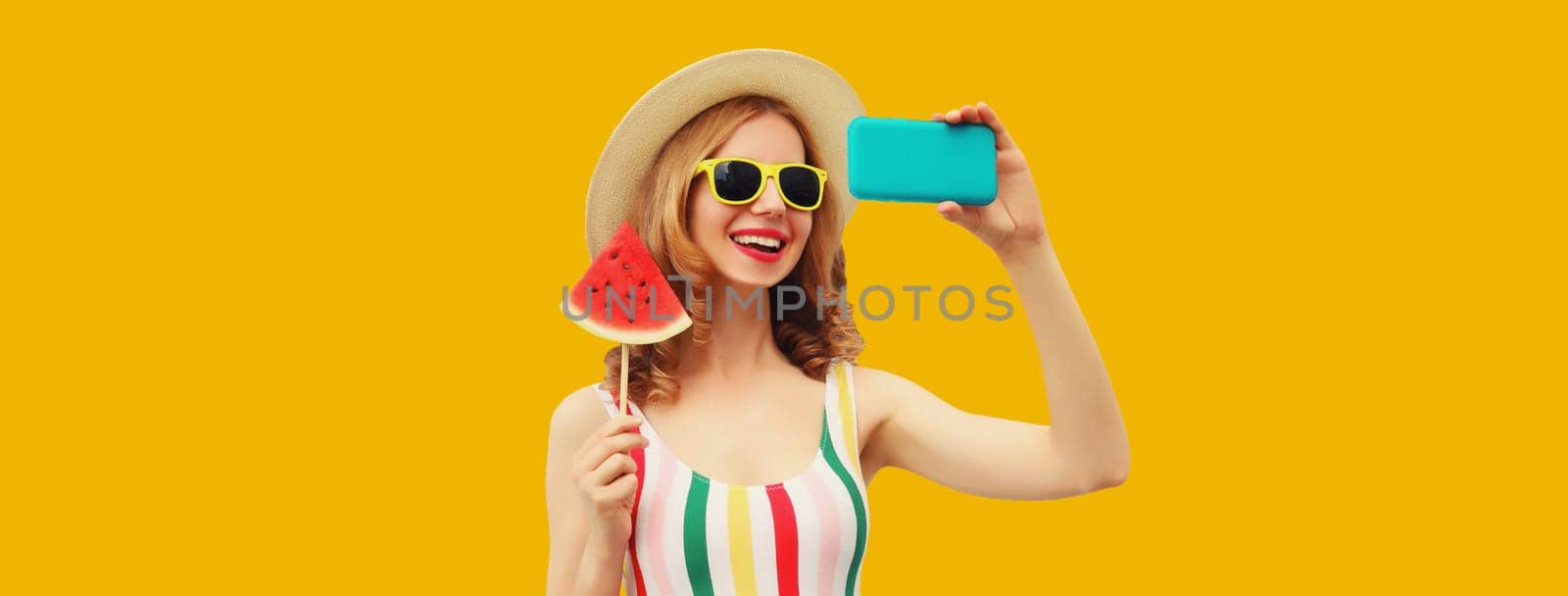 Summer portrait of cheerful happy laughing young woman taking selfie with phone and juicy lollipop or ice cream shaped slice of watermelon on bright orange background