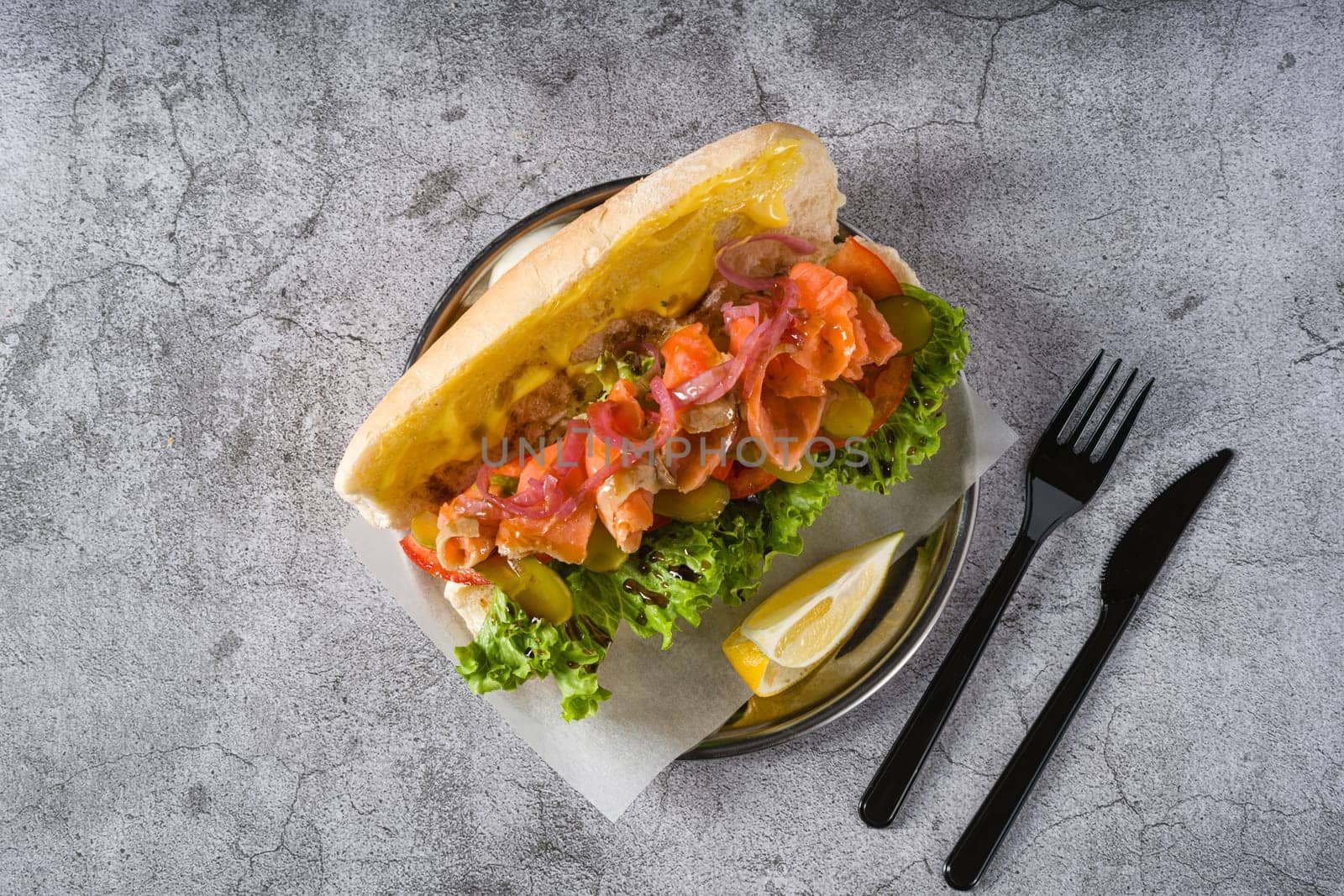 Smoked salmon sandwich on metal plate on stone table