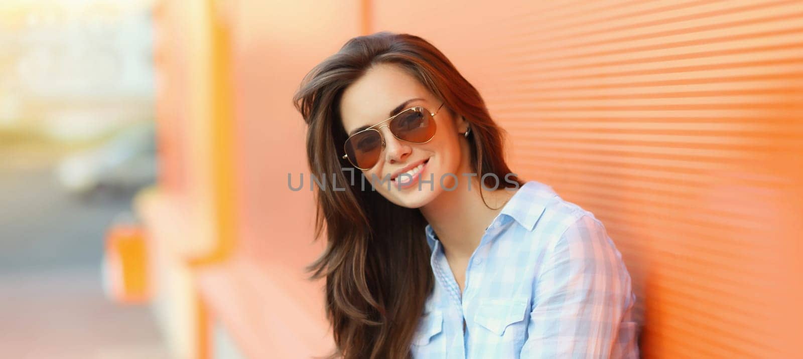 Portrait of beautiful happy smiling brunette young woman posing in the city on orange background