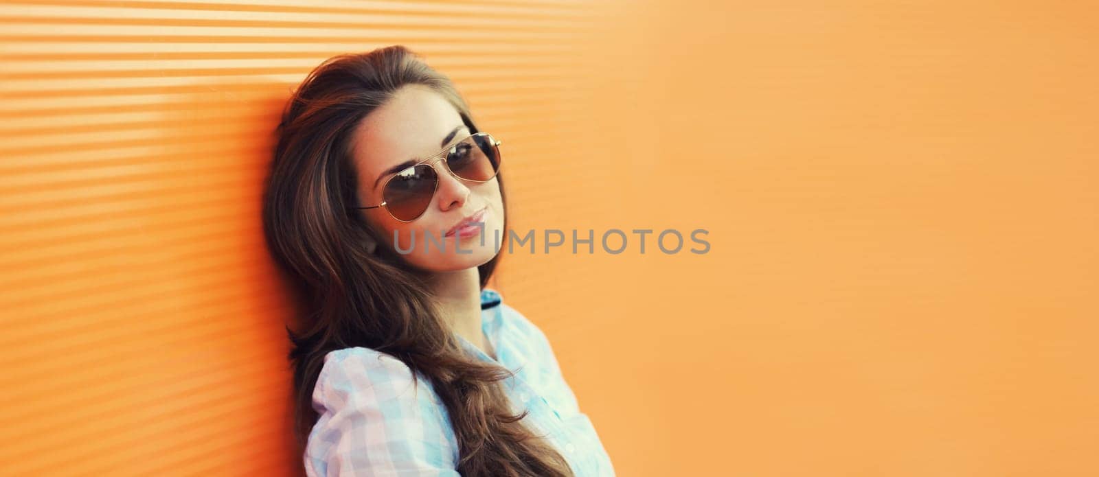 Portrait of beautiful brunette young woman in sunglasses posing in the city on orange background, copy space