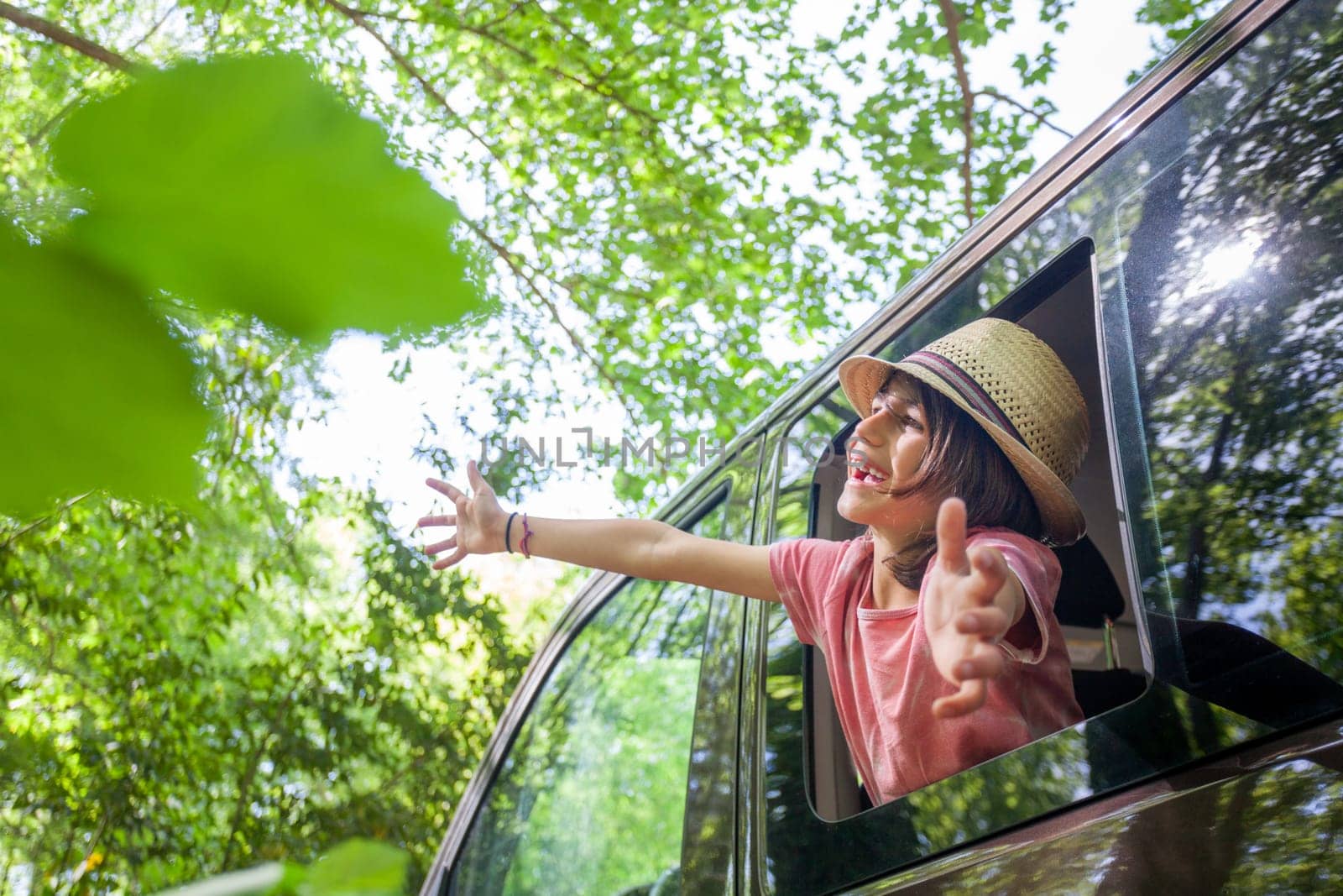 A young boy is sitting in a car window, smiling and waving by orafotograf