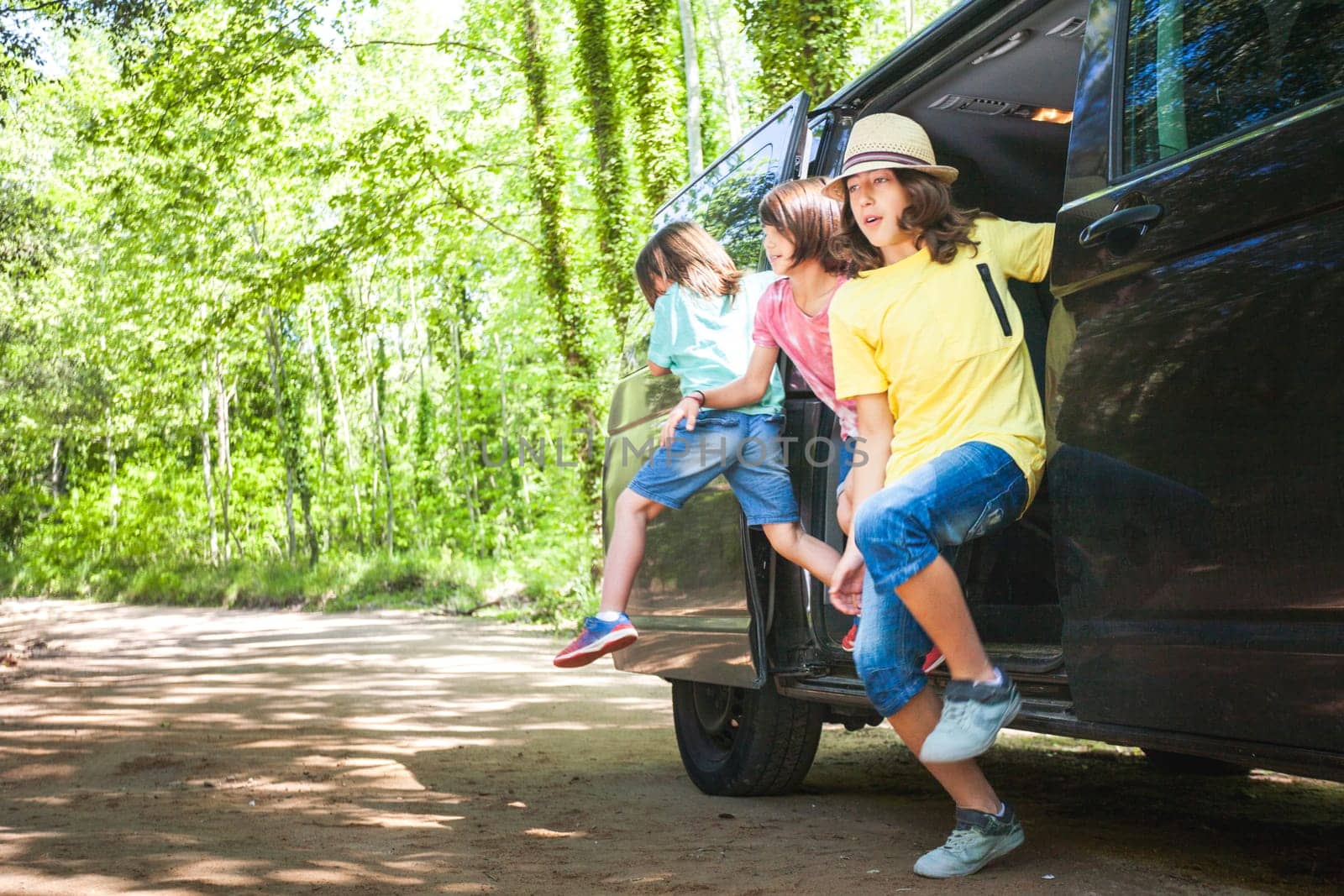 Three children run out of the side door of a van, in a forest on one of their outdoor days.
