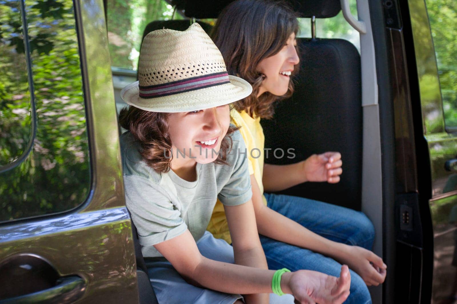 Two people are sitting in a van, one wearing a hat and the other wearing a yellow shirt. They are smiling and seem to be enjoying themselves