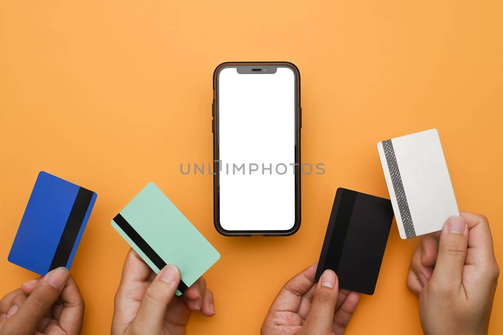 Hands holding credit cards near mobile phone on yellow background. Online shopping and modern payment systems concept.