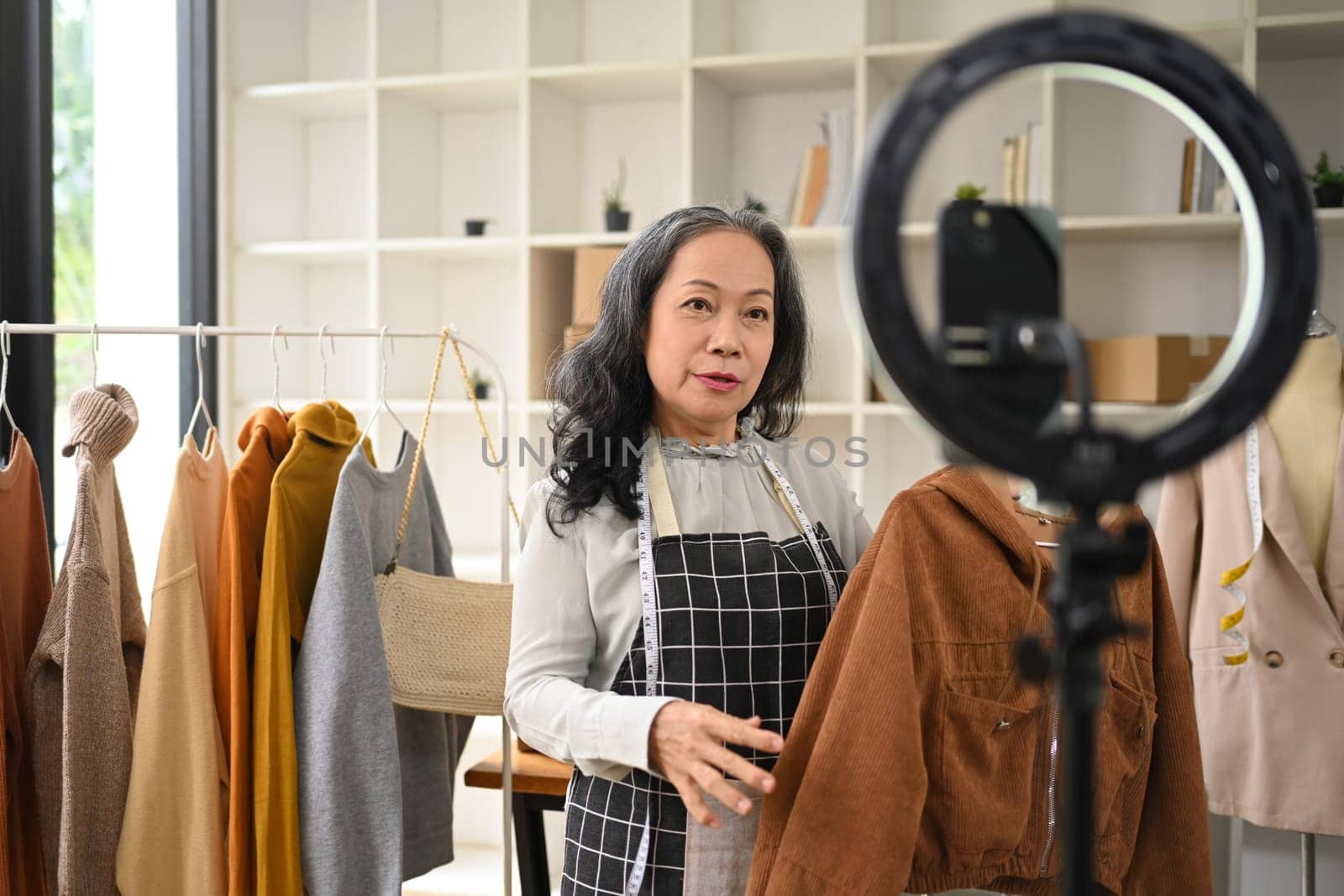 Middle age woman business owner showing new clothing during live streaming at her shop.