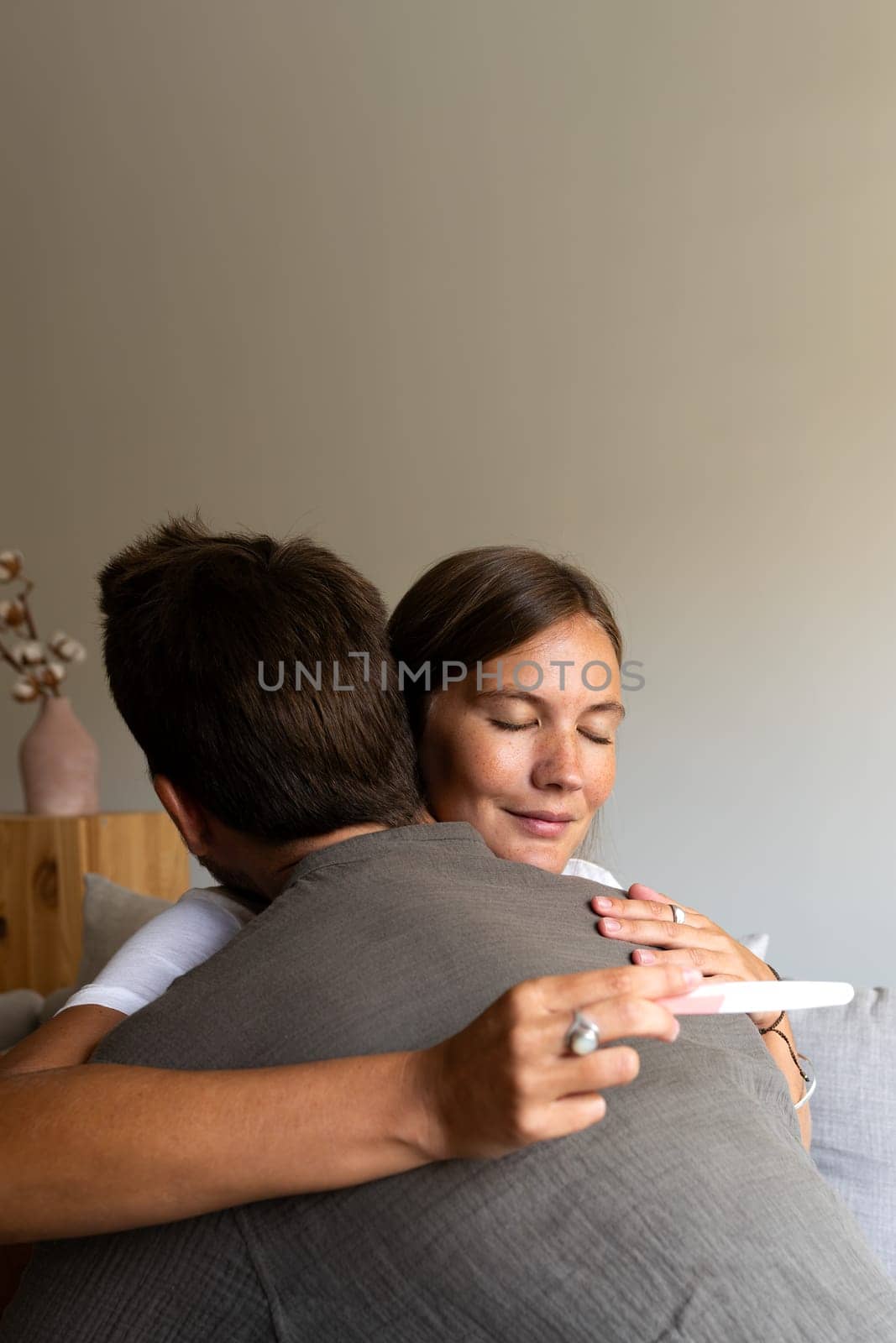 Vertical portrait of happy couple embrace celebrating positive pregnancy test result. Copy space. Love and family concept.