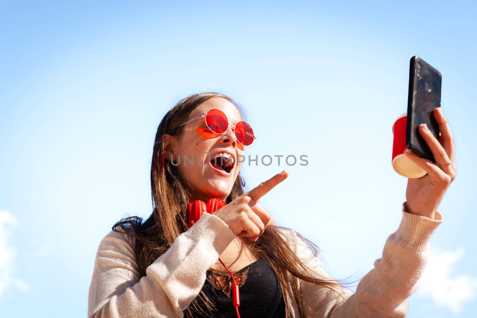Surprised caucasian woman points to her smartphone outdoors. by mariaphoto3