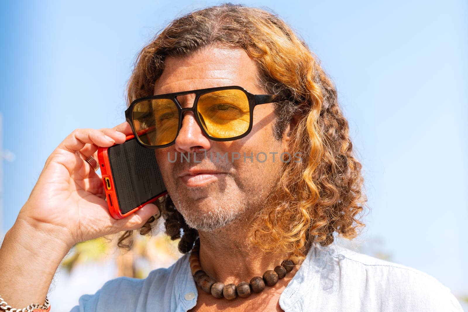 Caucasian man wearing sunglasses talks on cell phone and smiles outdoors