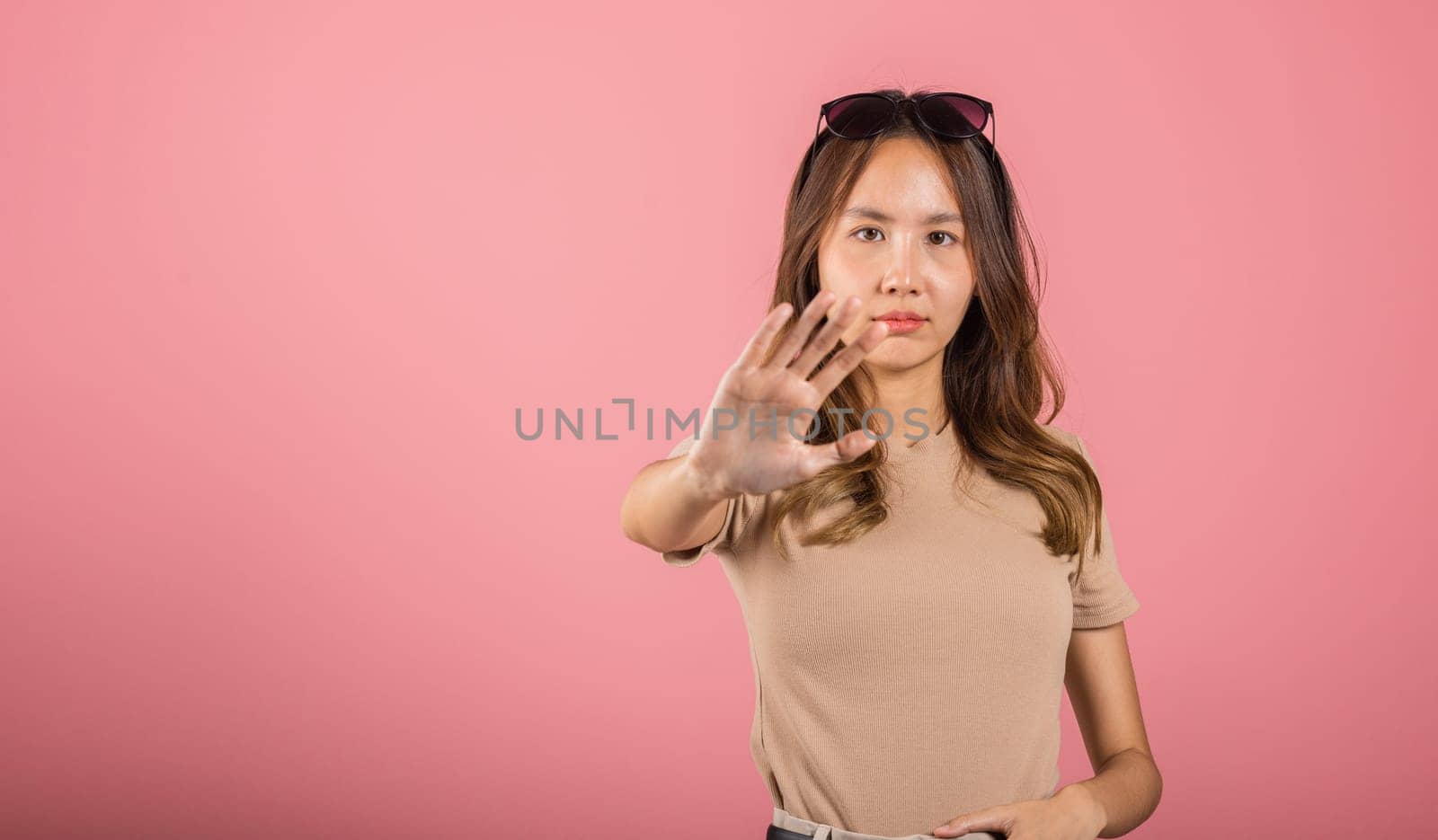 Asian beautiful woman itching her outstretched hand showing stop gesture front face on pink background with copy space, female doing show stop sign by Sorapop