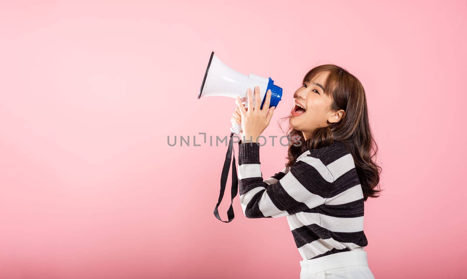 Portrait of happy Asian beautiful young woman teen confident smiling face holding making announcement message shouting screaming in megaphone, studio shot isolated on pink background by Sorapop