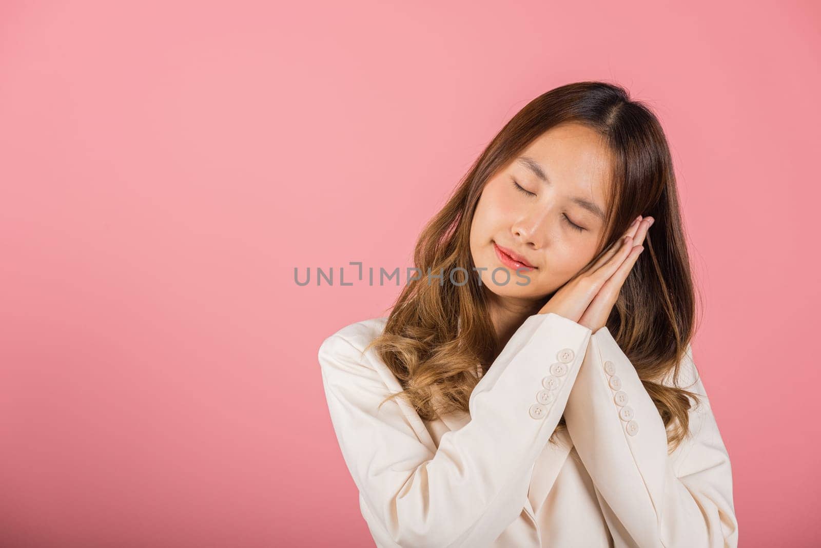 Portrait Asian beautiful young woman pretended emotions sleeping tired eyes closed dreaming with hands together near face, studio shot on pink background, with copy space by Sorapop