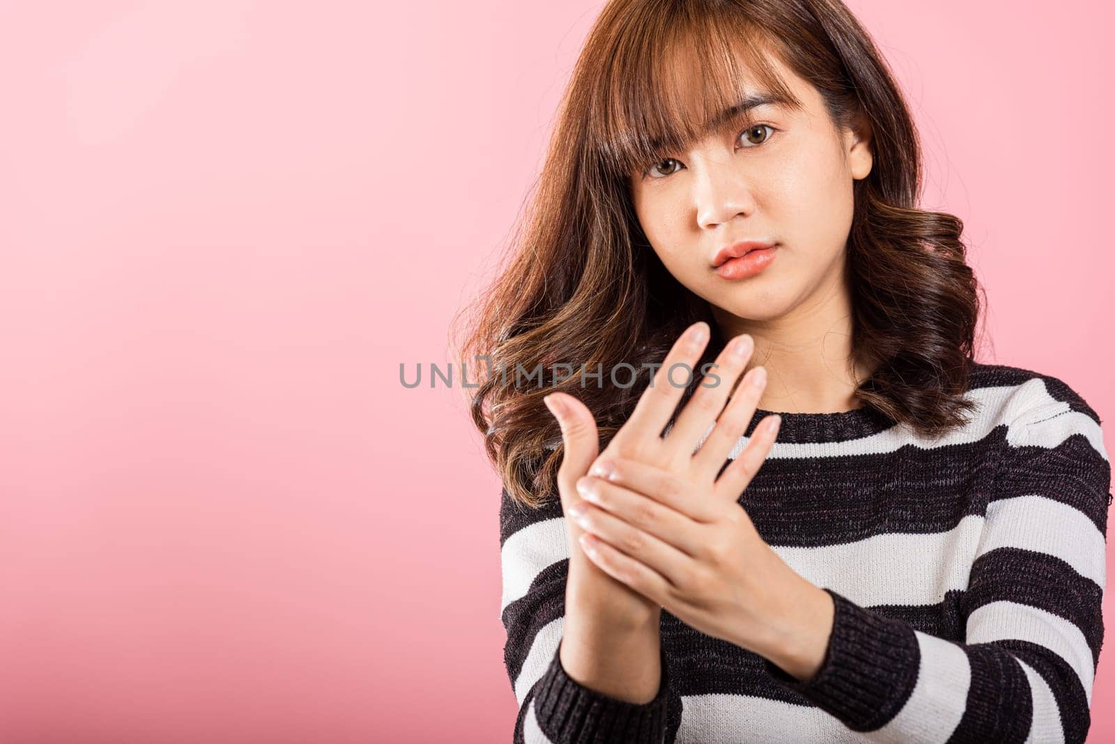 Portrait of Asian beautiful young woman suffering from pain in palm or hands and massaging her painful hands, studio shot isolated on pink background, Health care arthritis concept, Wrist pain