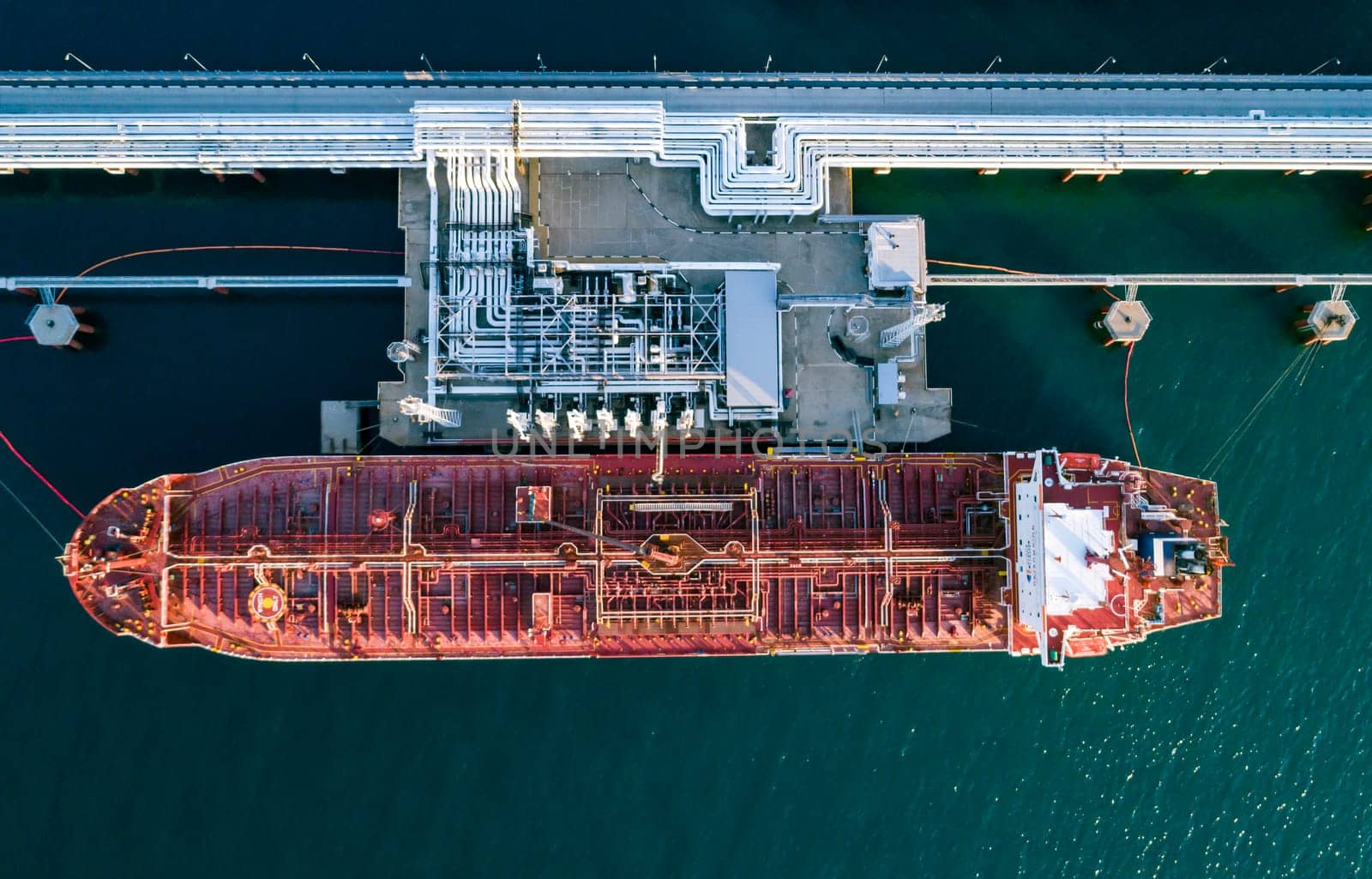 Aerial top down view of a large oil tanker docked at a pier in the port in process of loading.