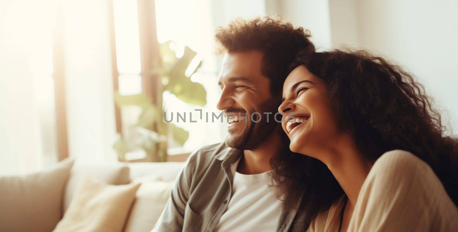 Portrait of happy smiling young couple hugging, cheerful laughing woman and man sitting on sofa at home together