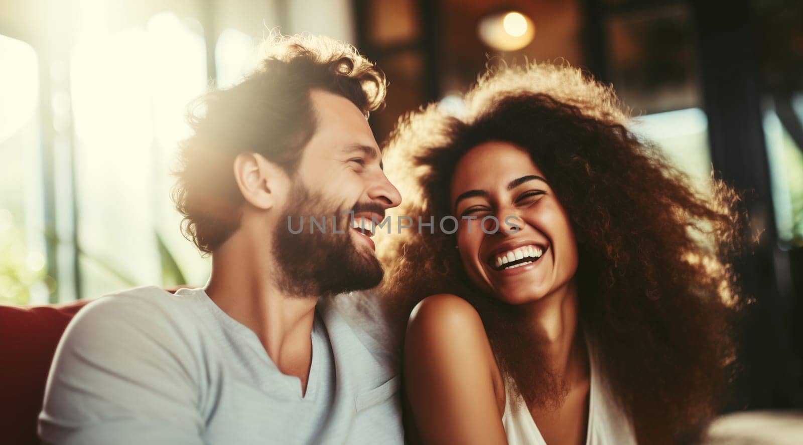 Portrait of happy smiling young couple hugging, cheerful laughing woman and man sitting on sofa at home together