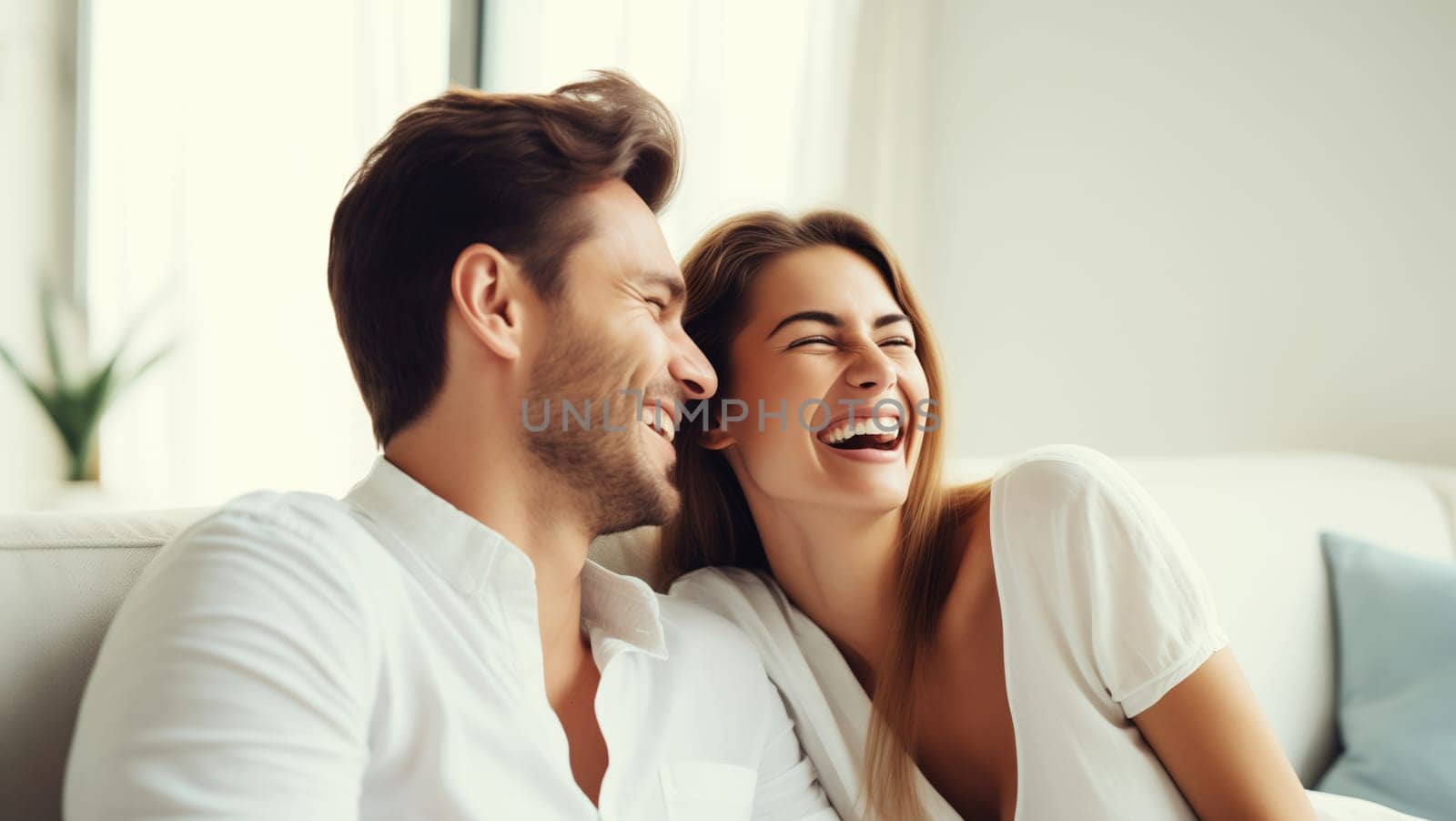 Portrait of happy smiling young couple hugging, cheerful laughing woman and man sitting on sofa at home together