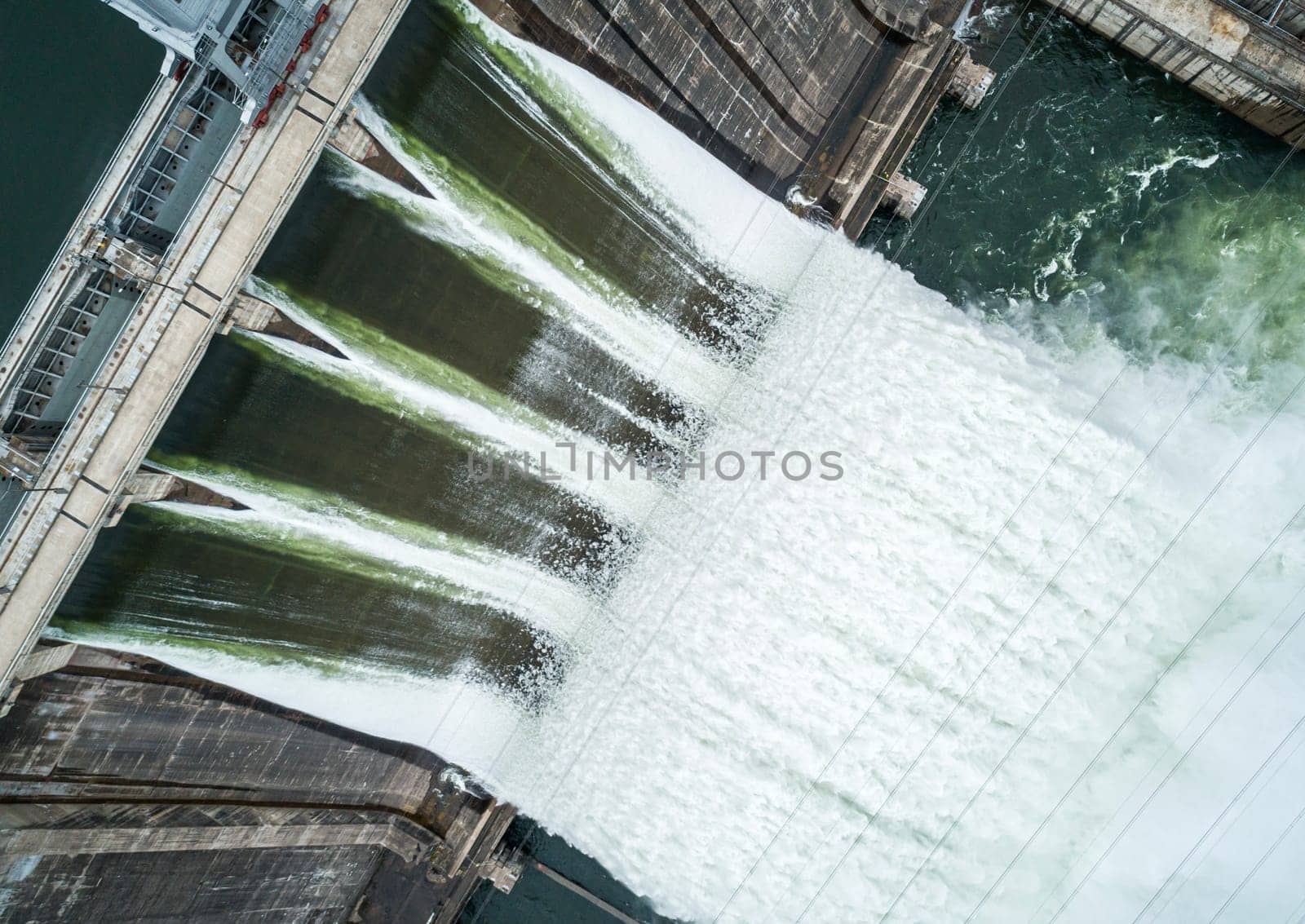 Aerial top down view of concrete dam releasing water into river on cloudy day. Water discharge at hydroelectric power plant.