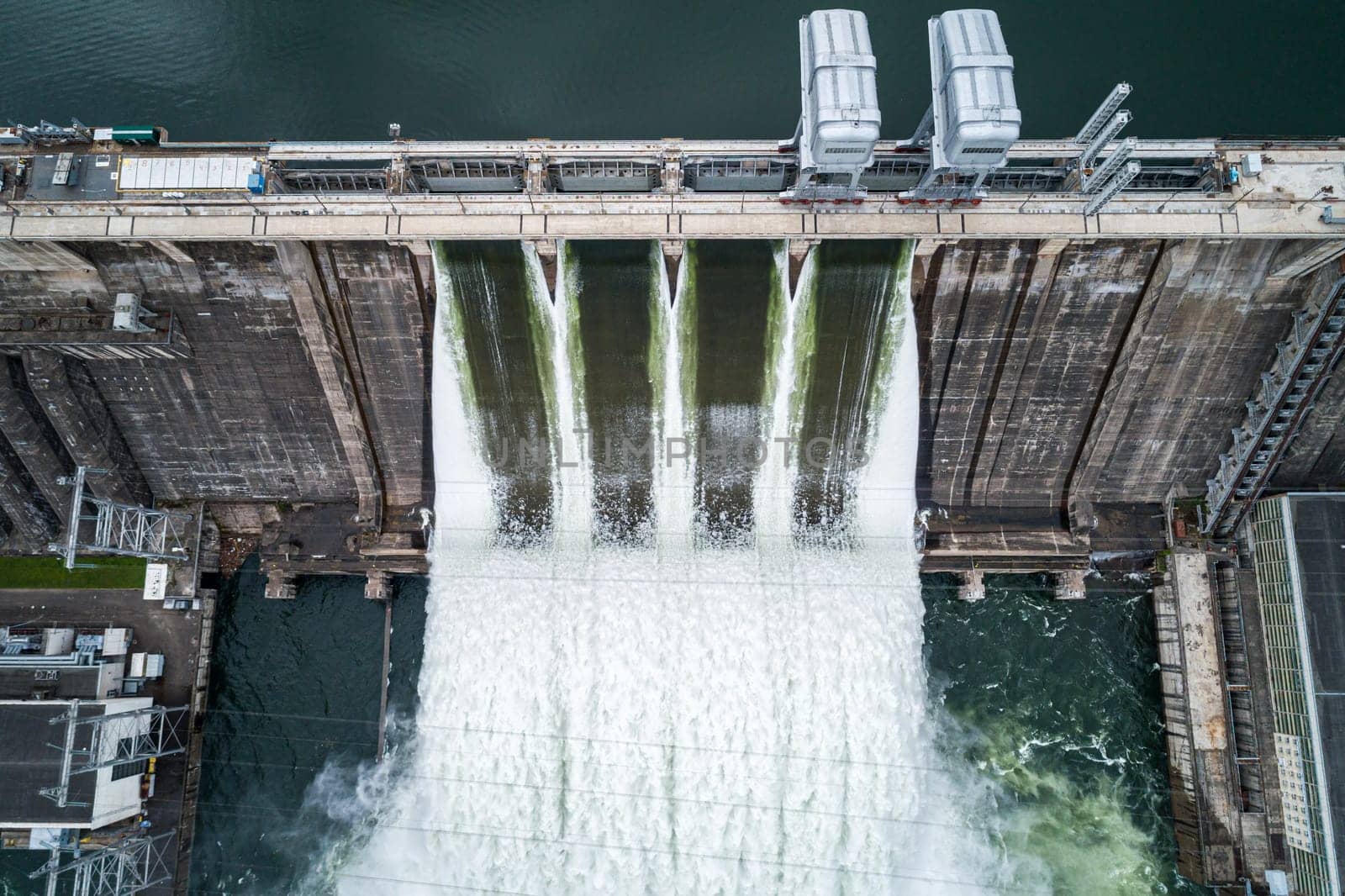 Aerial top down view of concrete dam releasing water into river on cloudy day. Water discharge at hydroelectric power plant. by Busker