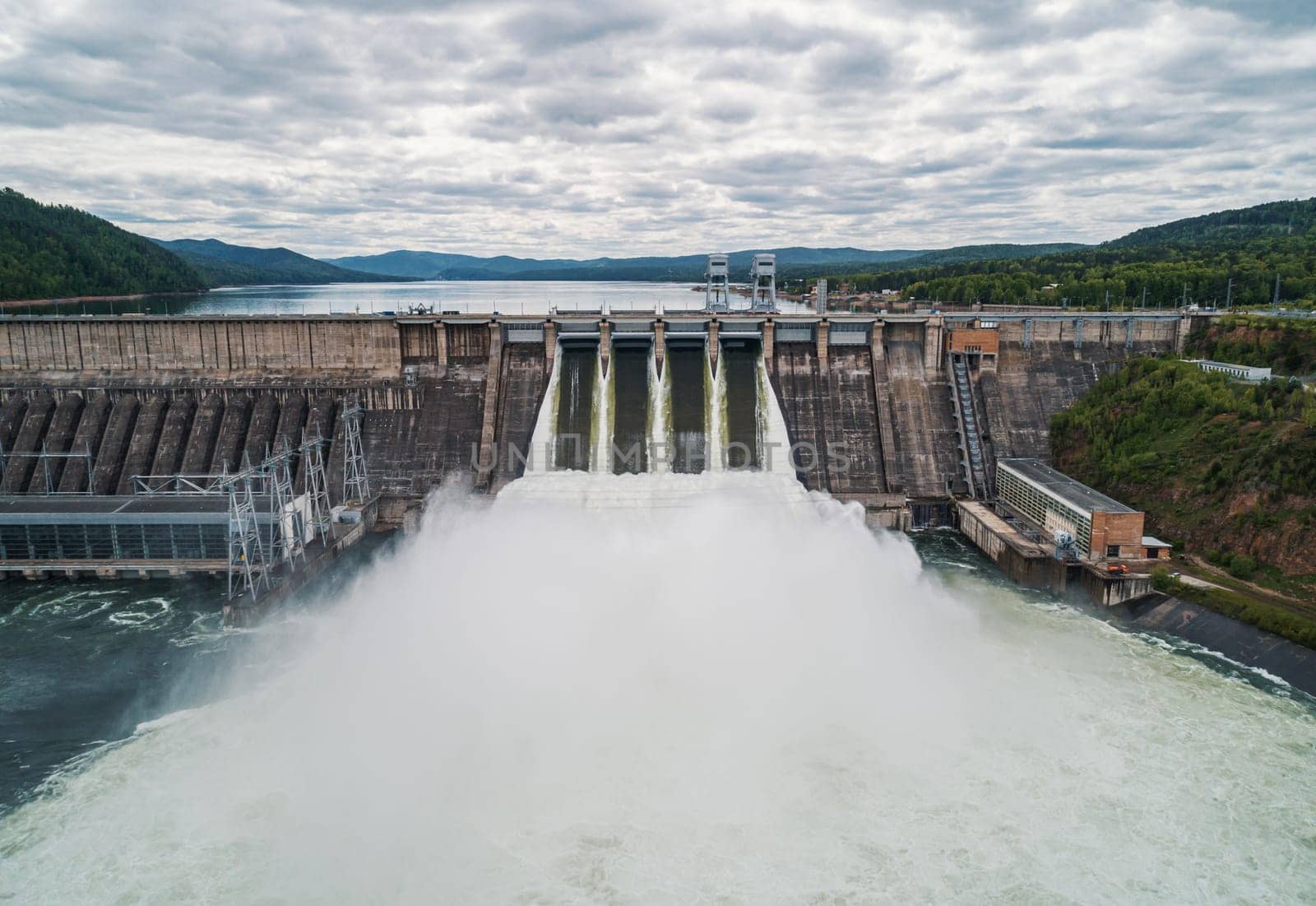 Aerial view of concrete dam releasing water into river on cloudy day. Water discharge at hydroelectric power plant. by Busker