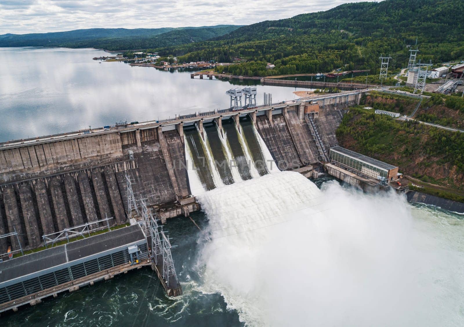 Aerial view of concrete dam releasing water into river on cloudy day. Water discharge at hydroelectric power plant. by Busker