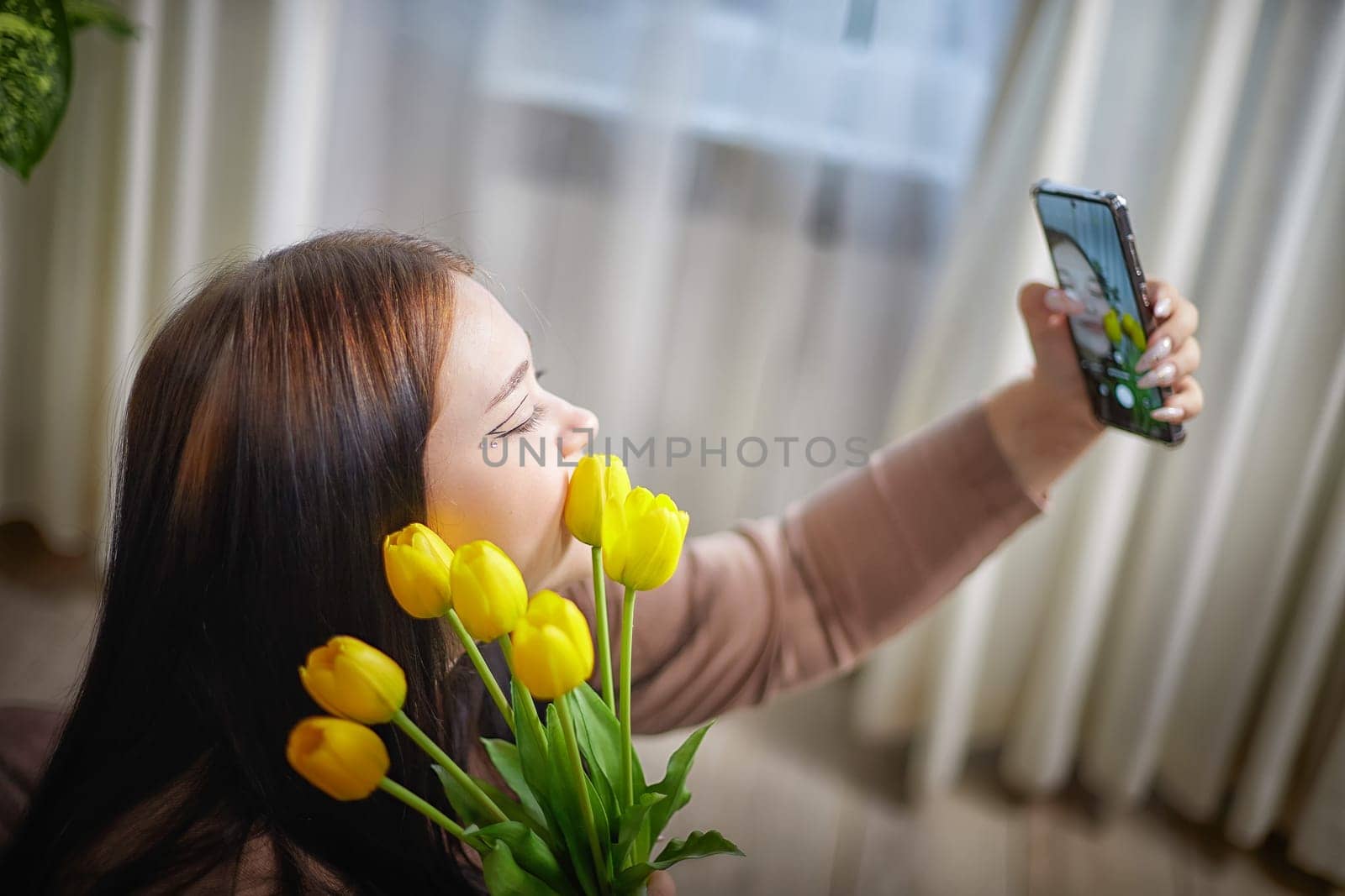 happy stylish fat plumb brunette girl making selfie with yellow tulips in room. happy young lady on International women's day, young hipster woman