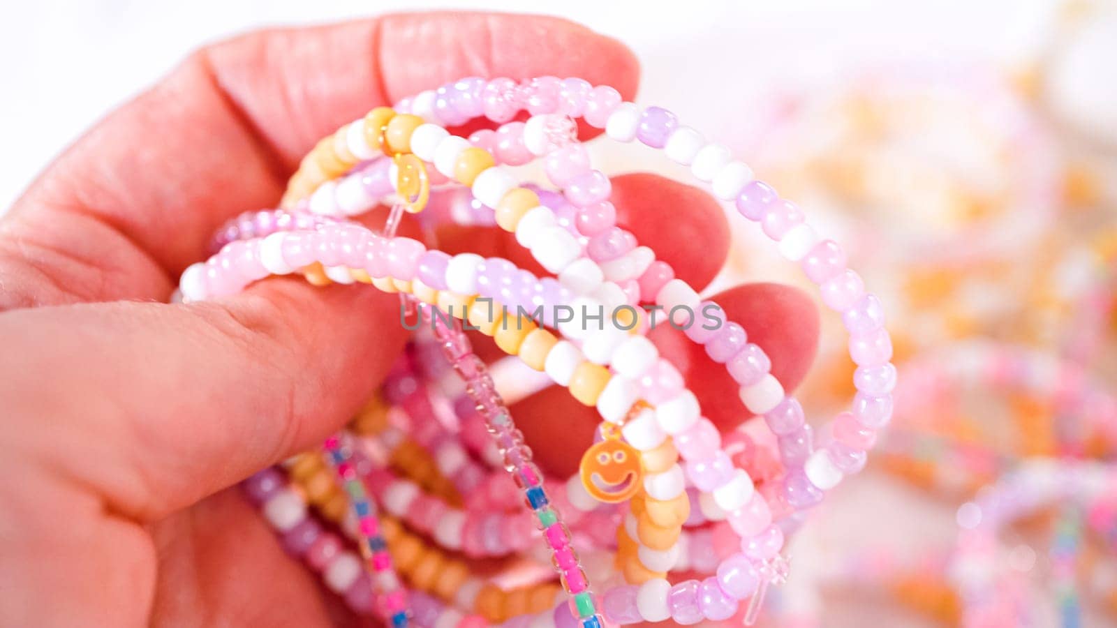 Delicate fingers of a young girl navigate through a treasure trove of bright, multicolored beads, each compartment revealing a new hue to choose from. She's immersed in the joyful task of stringing together a handmade bracelet, with golden beads and pearls lying nearby to add a touch of sparkle to her creation.