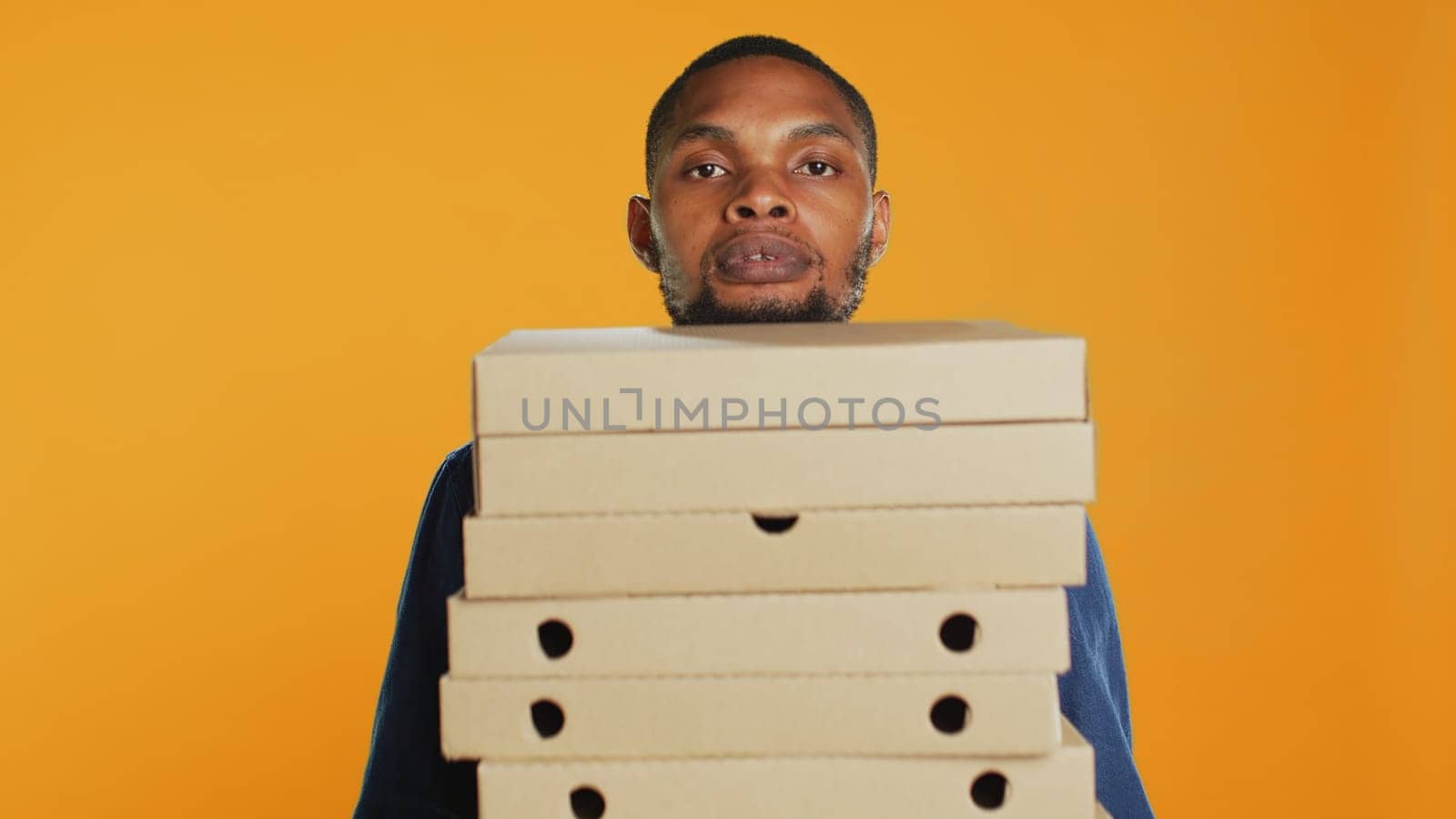 Clumsy deliveryman dropping a huge stack of pizza boxes in studio, wasting a lot of food and making a mess. Young distressed man makes a mistake and spills a large pile of fast food. Camera A.