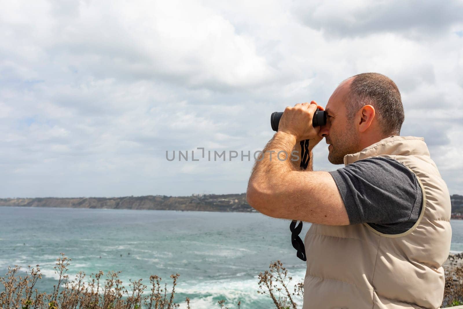 Mockup Mature Man, Adult Looks Into Distance Through Binoculars At Sea, Ocean Shore. Blue Sky, Water On Background. Summer Vacation, Hobby. Handsome 40 Yo Caucasian Male Explores Nature During Trip.