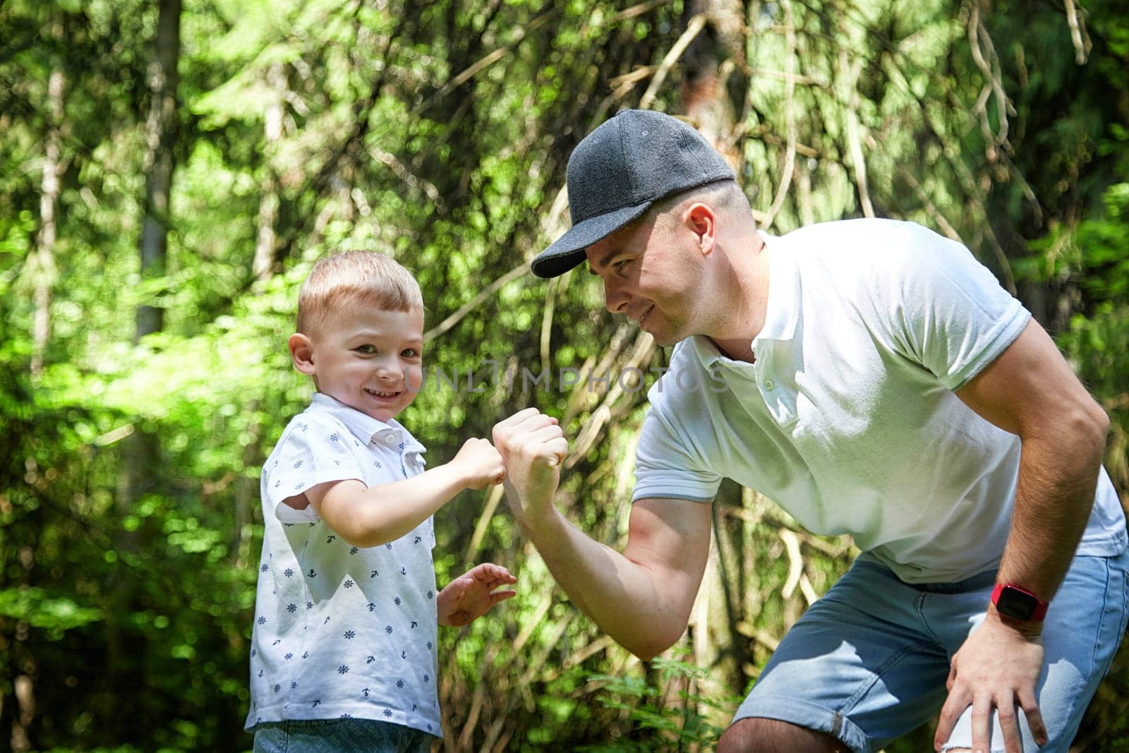 Father and Son Enjoying Playful Fist Bump in Lush Forest. A joyful moment as a dad and his young son exchange a fist bump in the woods