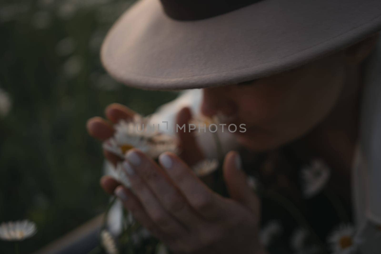 A woman wearing a hat is smelling flowers. The flowers are white and are scattered around her. The scene has a peaceful and calming mood