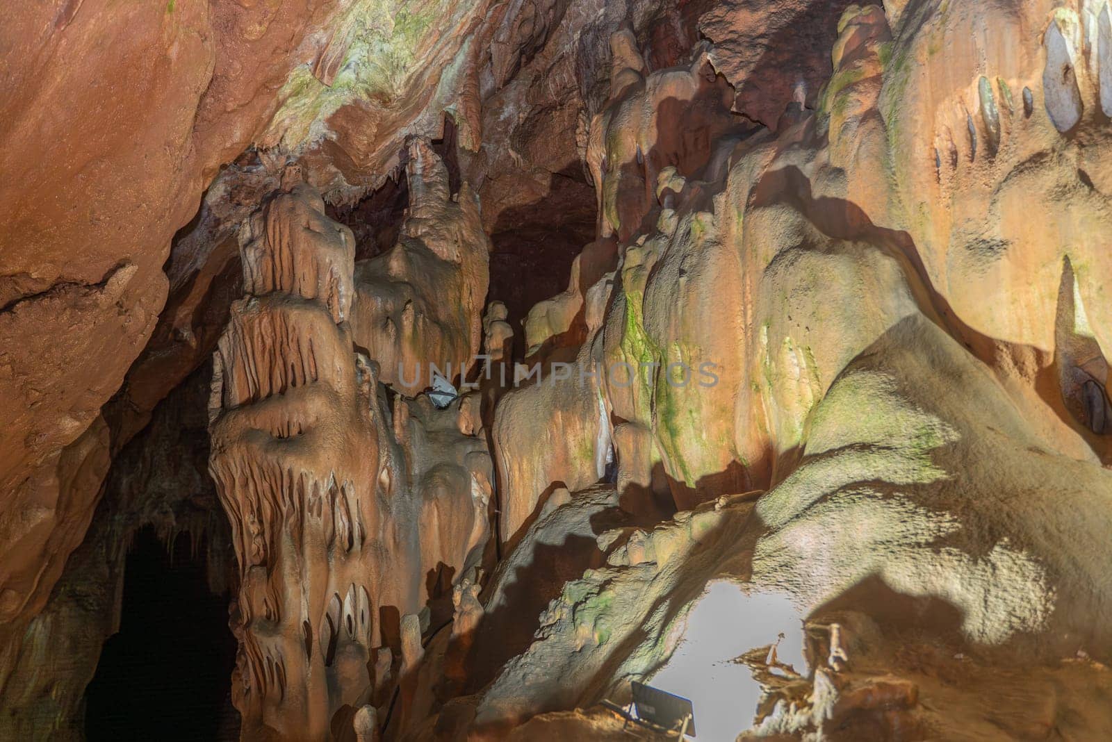 A cave with many stalactites and stalagmites. The cave is dark and the light is coming from the outside