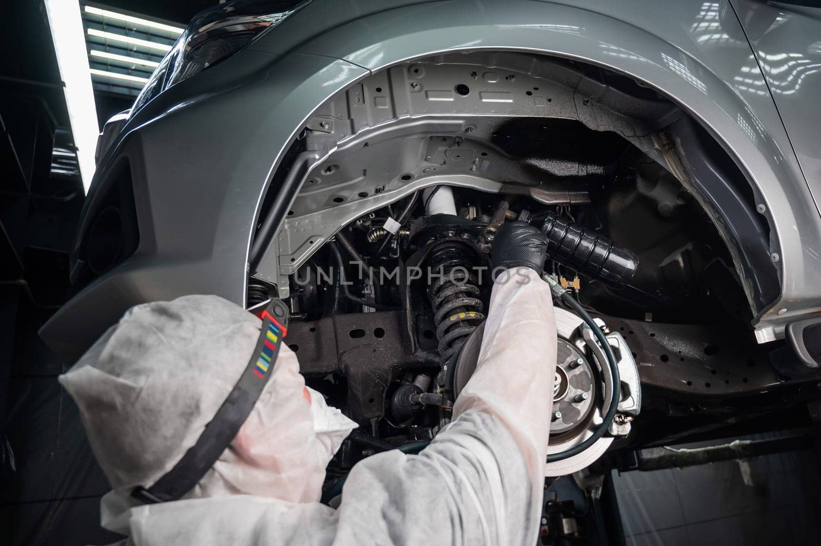 An auto mechanic applies anti-corrosion mastic to the underbody of a car