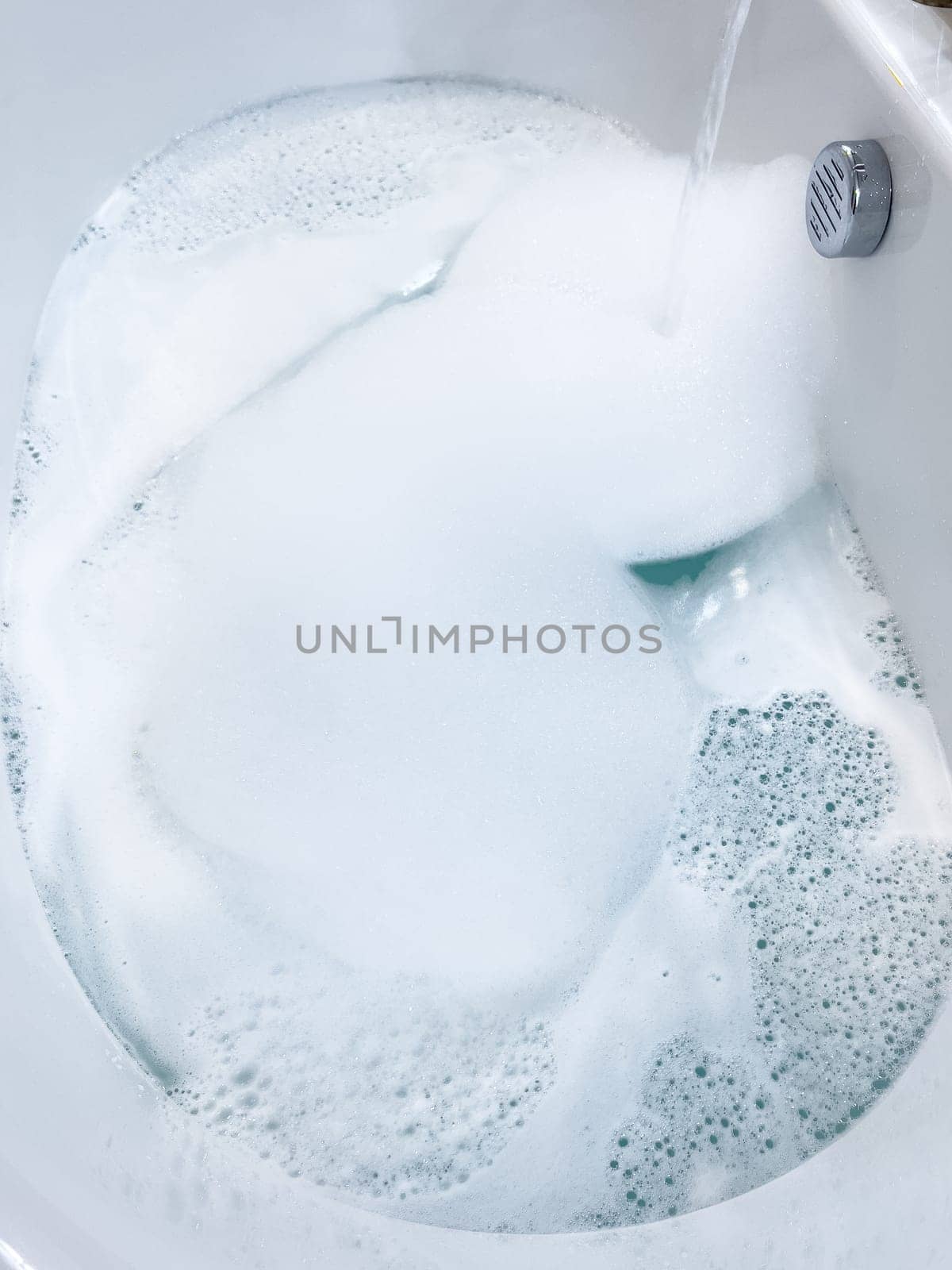 Modern White Bathtub Filled with Running Water from a Brushed Nickel Faucet by arinahabich