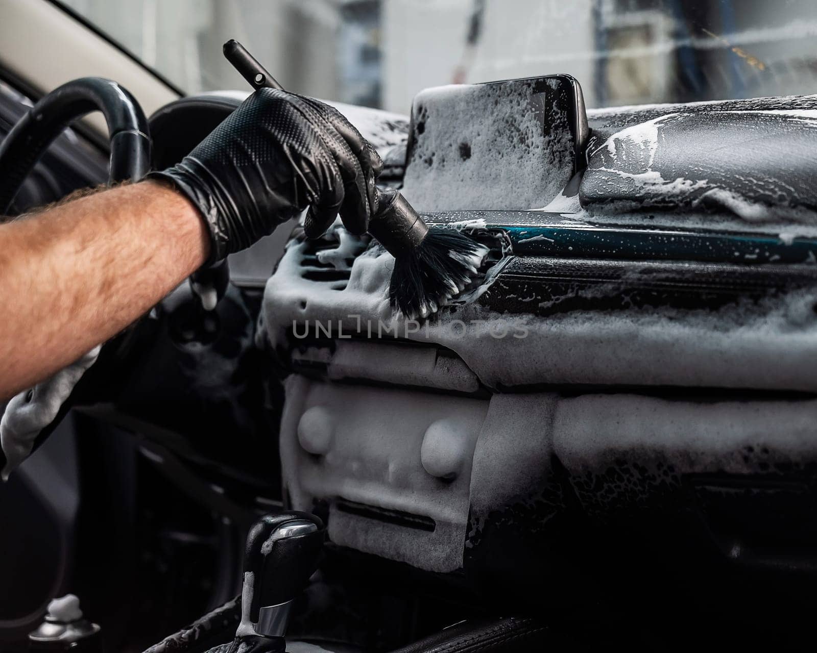 A mechanic cleans the interior of a car with a brush and foam. by mrwed54