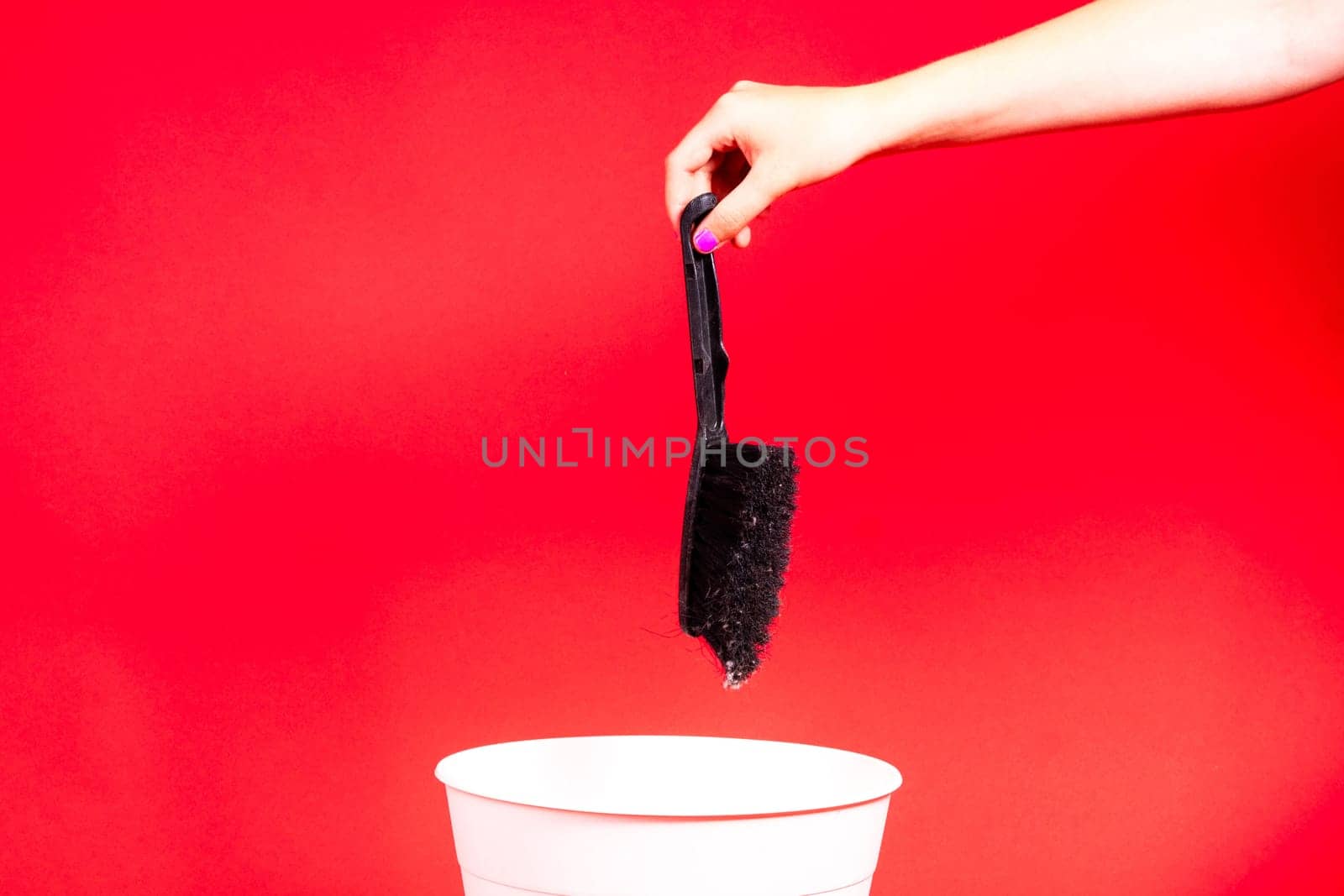 Hand throws brush into trash bin with package on red background by Zelenin