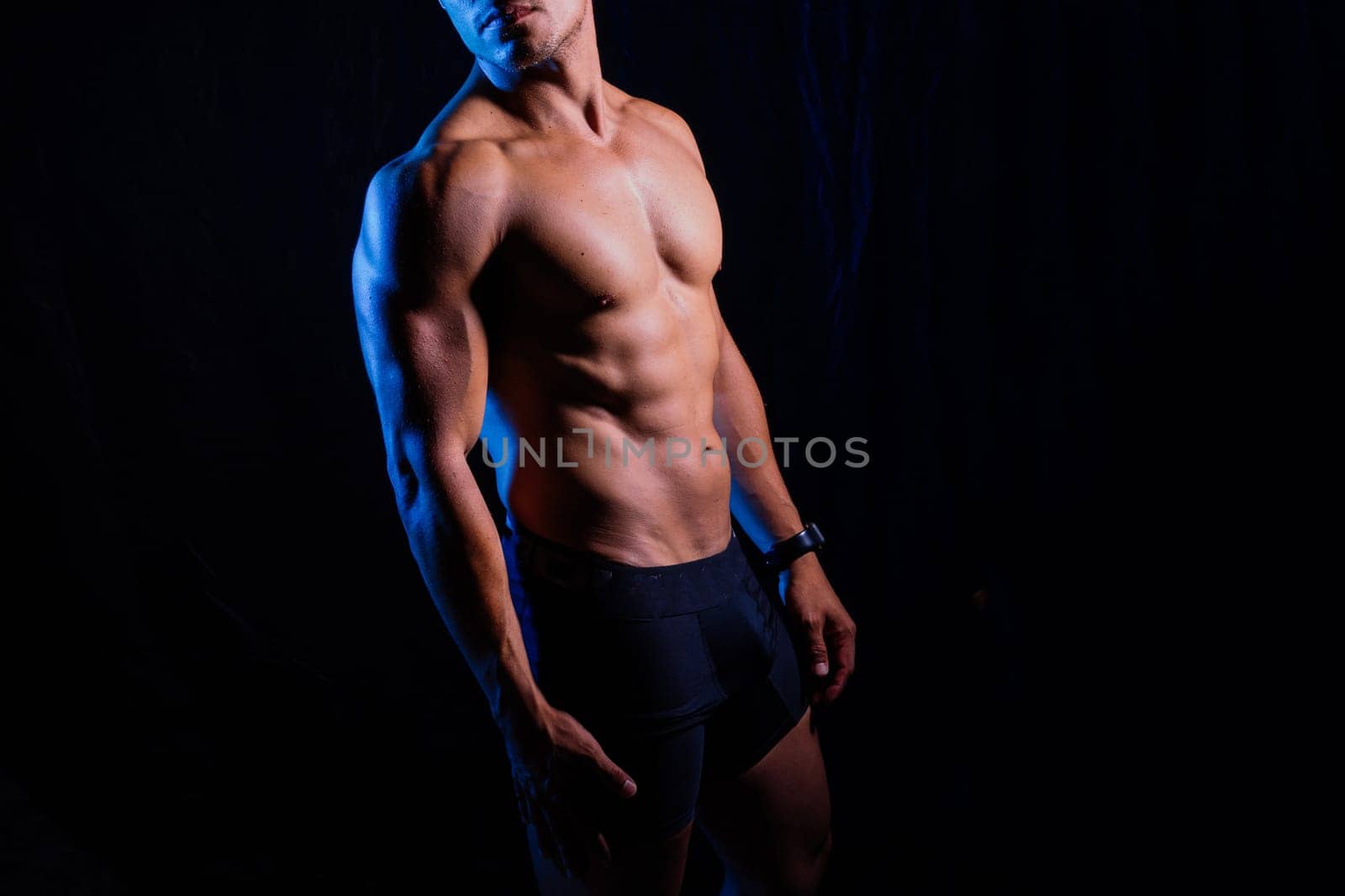 Man with exposed torso poses against black backdrop for flash photography by Zelenin