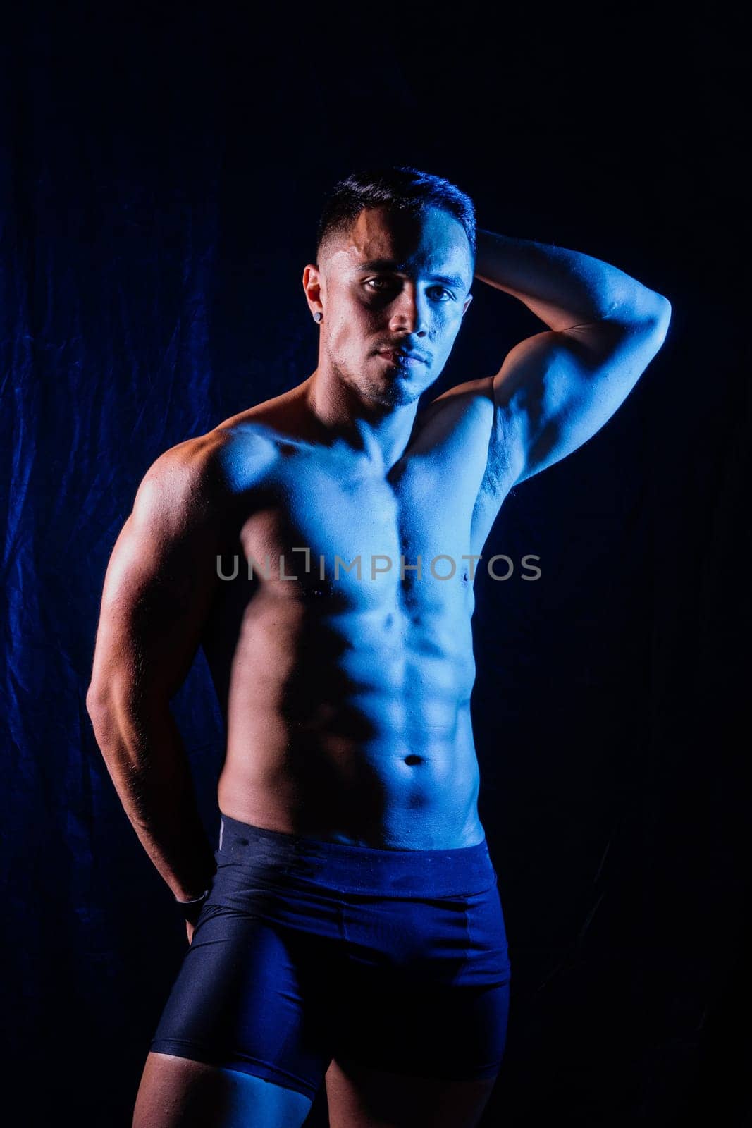 Man with exposed torso poses against black backdrop for flash photography by Zelenin
