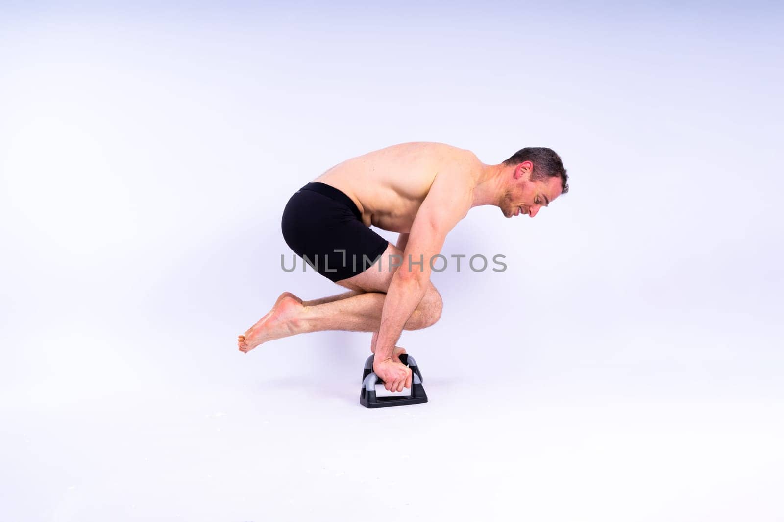 Shirtless muscular athlete doing push-up on push up bars. Full body man on white studio background. by Zelenin