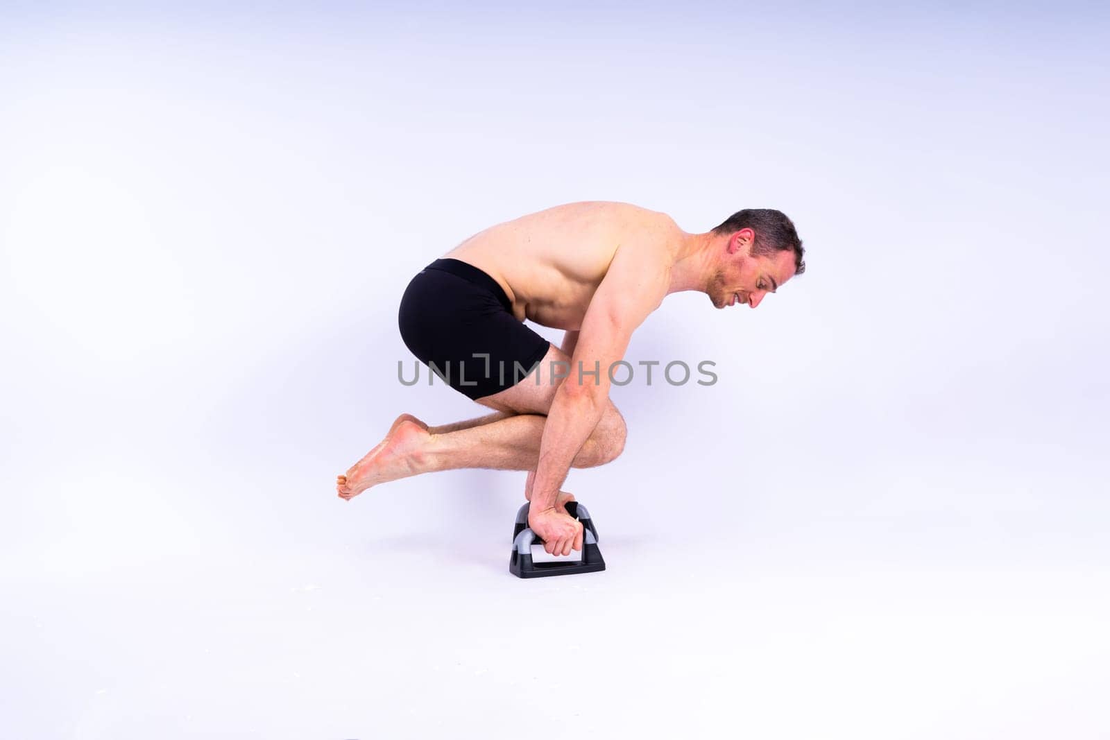 Shirtless muscular athlete do push-up on push up bars. Full body man on white studio background.