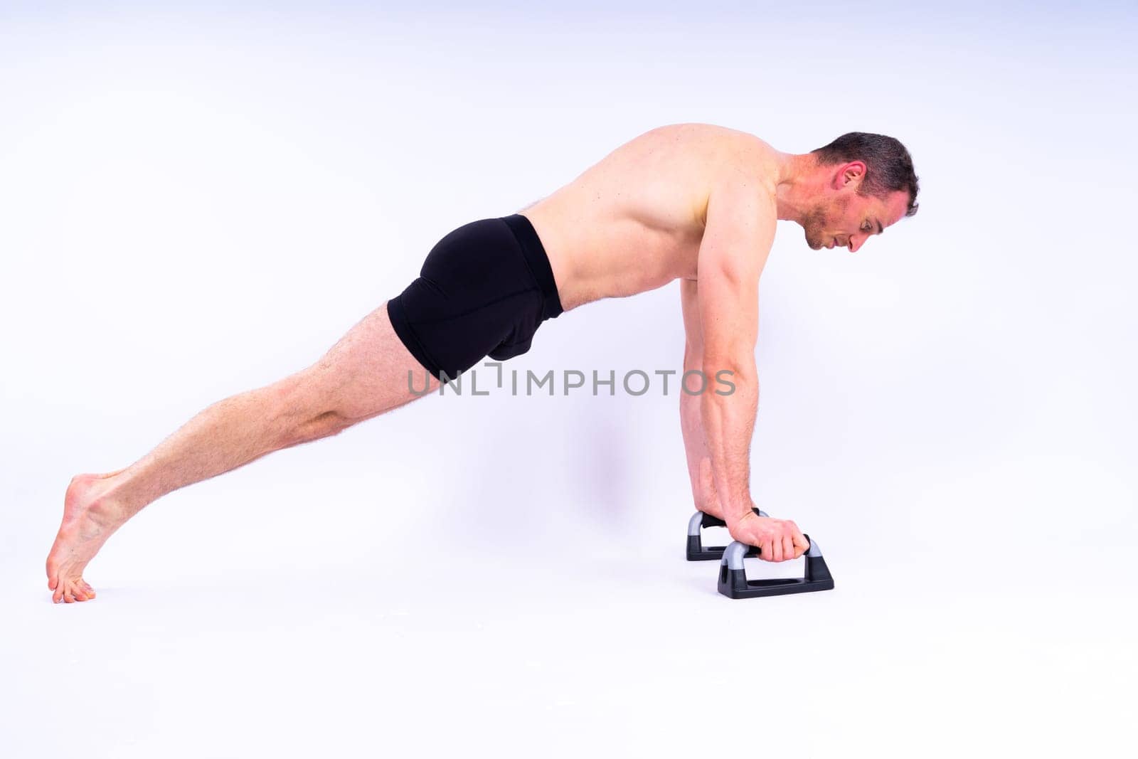 Shirtless muscular athlete do push-up on push up bars. Full body man on white studio background.