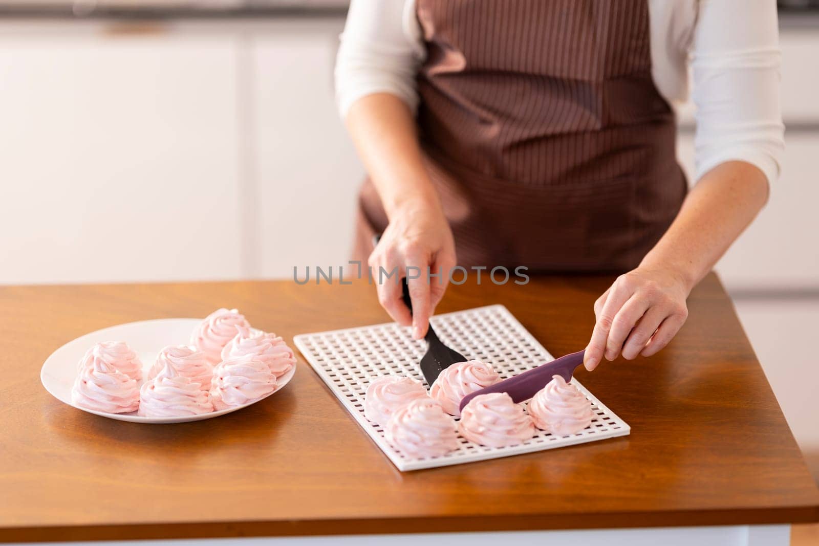 A woman is cutting a tray of pink pastries on a wooden table. The pastries are arranged in a grid pattern on the tray