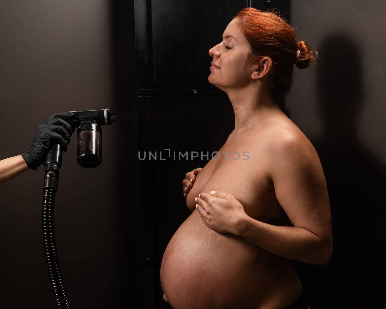Pregnant woman getting an instant tan. The master applies bronzer with a spray