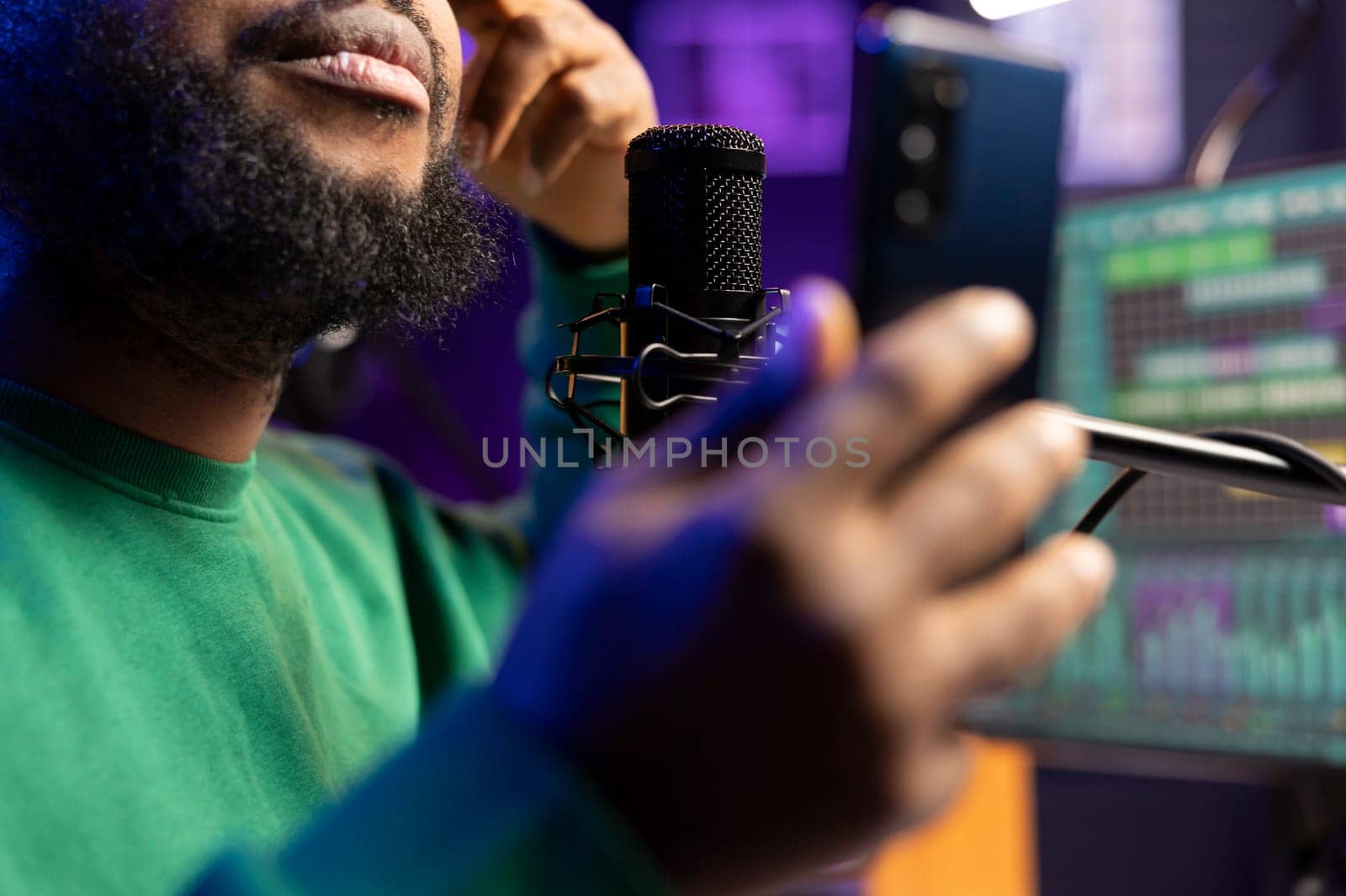 Artist composer singing an acoustic version of his latest song, live recording session on microphone in home studio. Songwriter producing new music, reading verses on his phone. Close up.