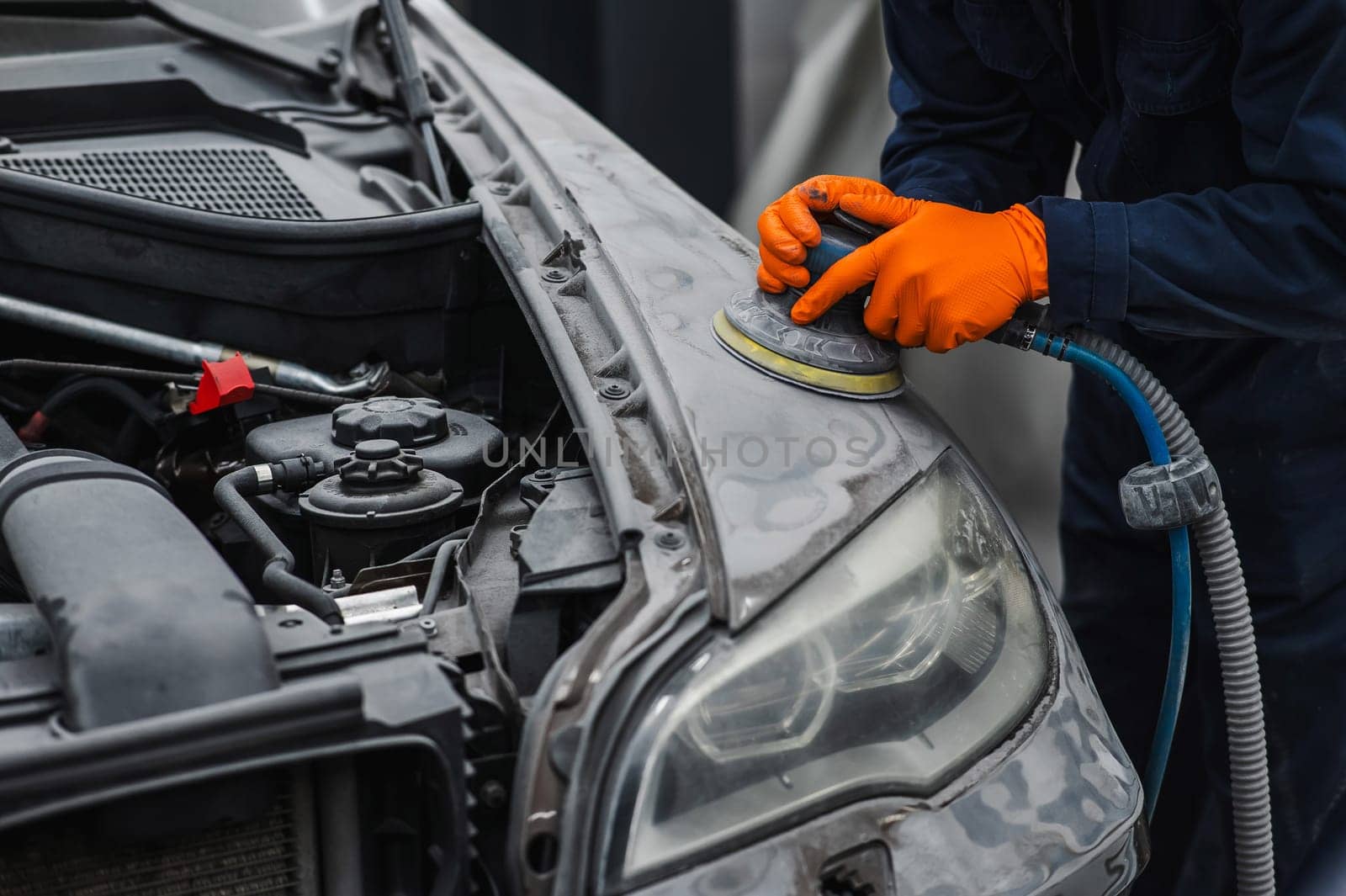 A mechanic sands the putty on a car body with a machine. Repair after an accident