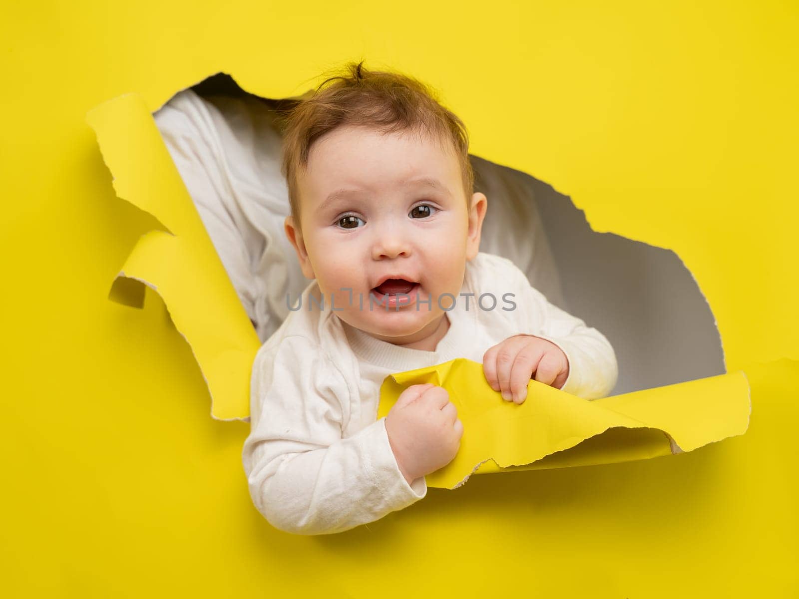Cute Caucasian baby sticking out of a hole in a paper yellow background. by mrwed54