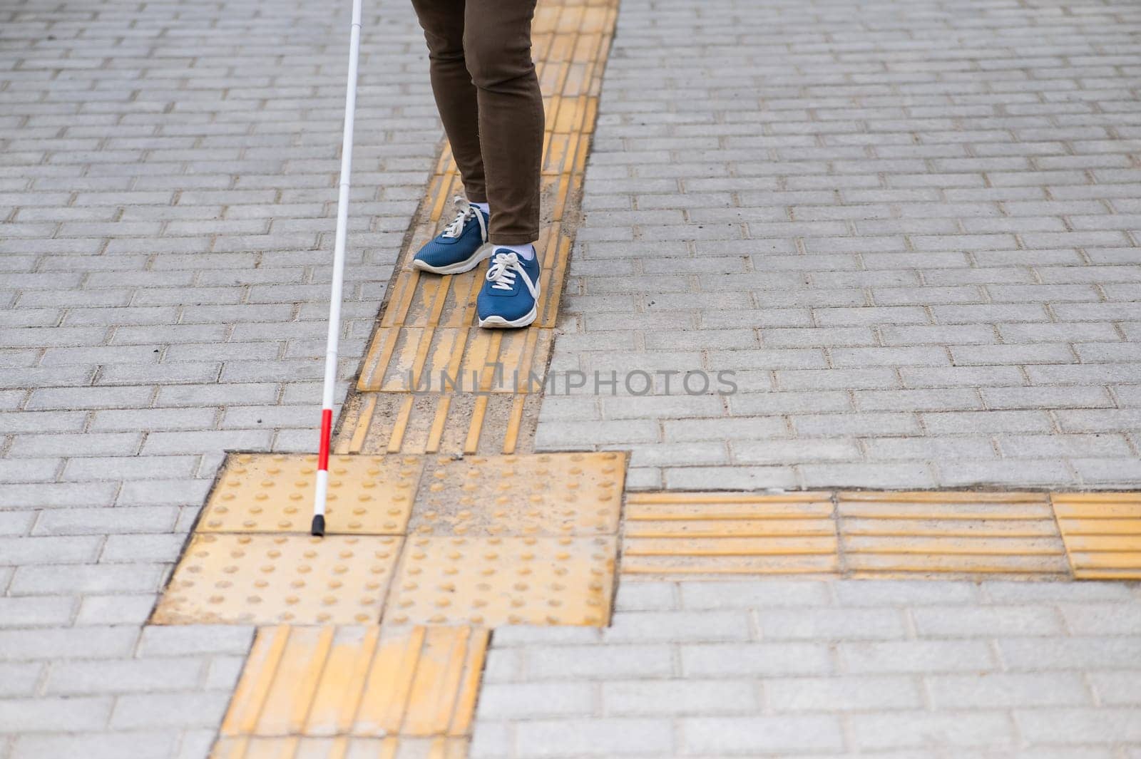 Close-up of a woman's legs with a cane near a tactile tile. by mrwed54