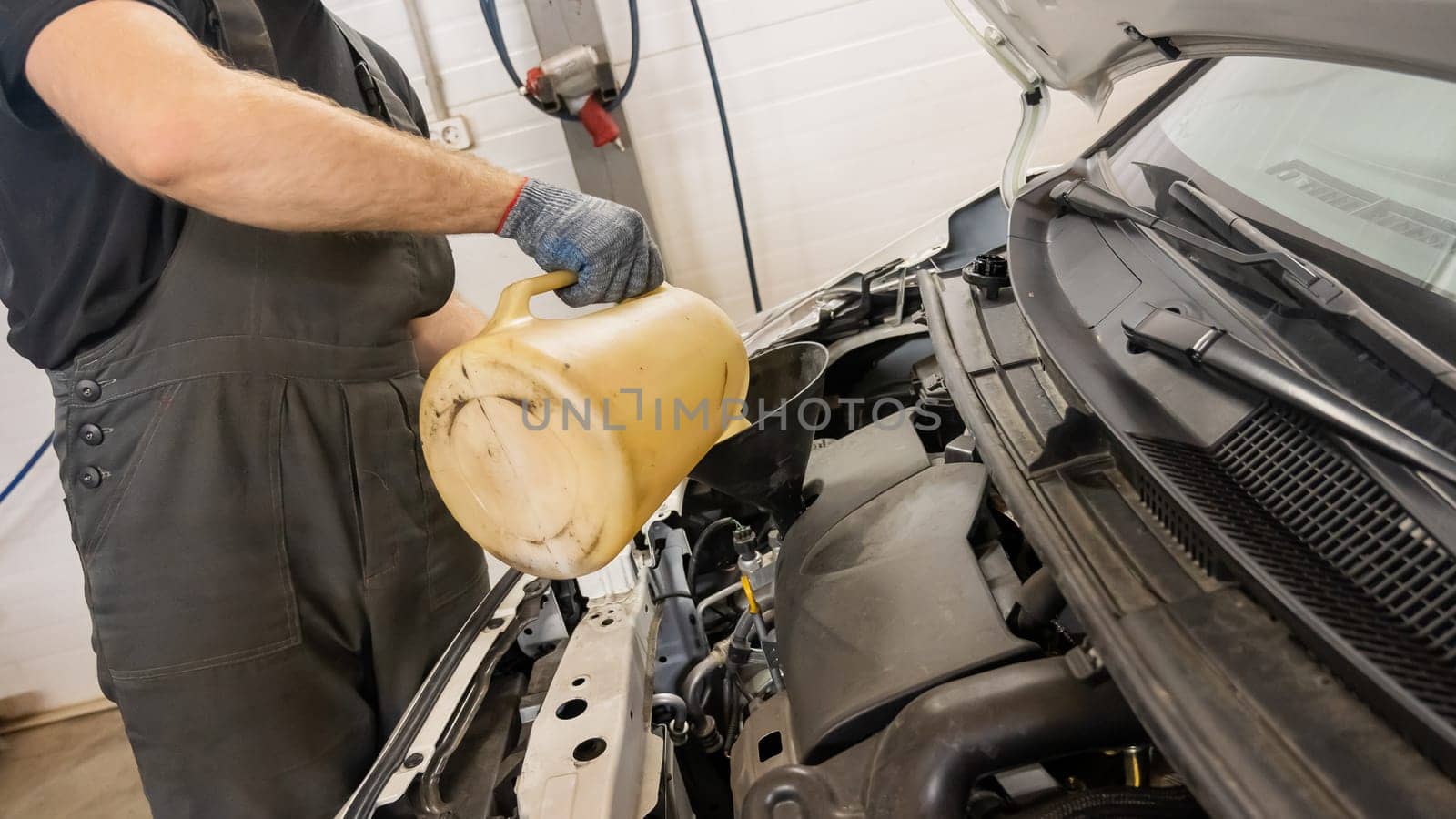 A mechanic fills a car engine with oil. Close-up of a man's hands