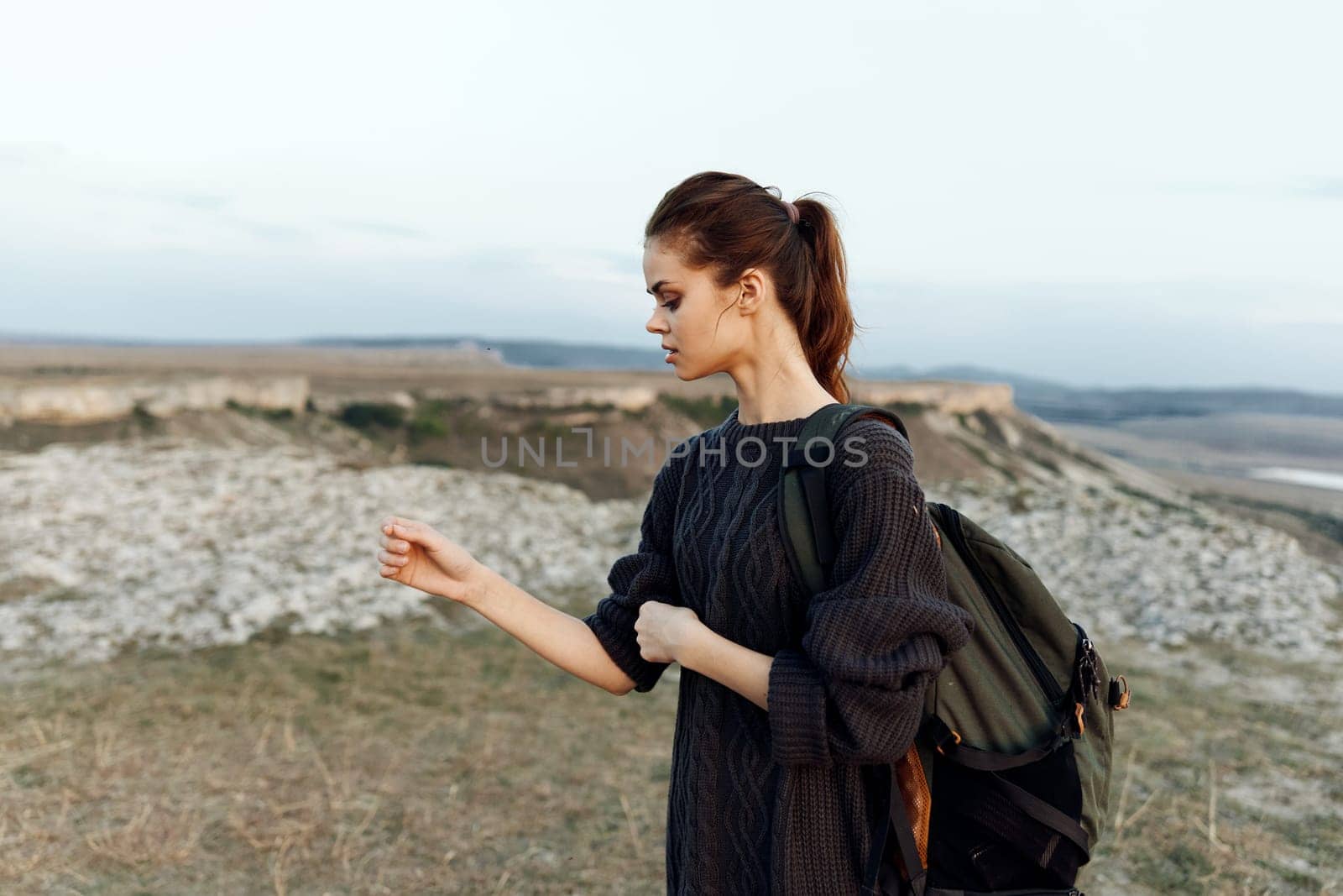 adventurous woman standing on hilltop with backpack, enjoying scenic landscape view